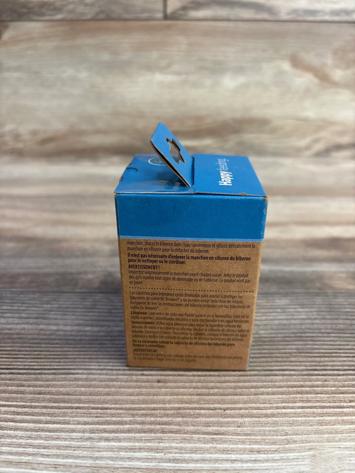 Rear view of Dr. Brown's narrow silicone glass bottle sleeve in its blue and brown retail box with hang tab on wooden surface