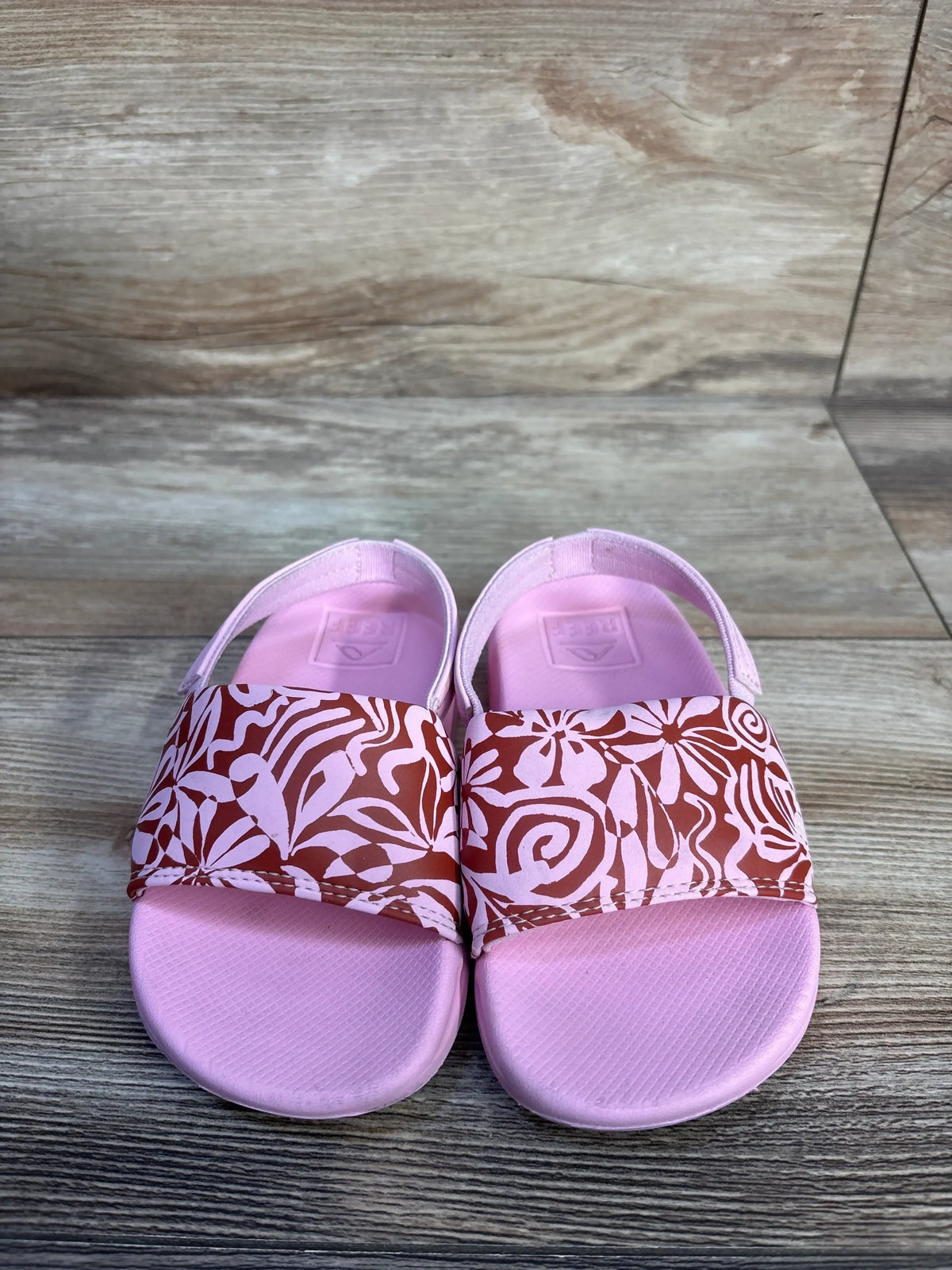 Pair of pink Reef modern floral sandals for kids size 9c on a wooden surface