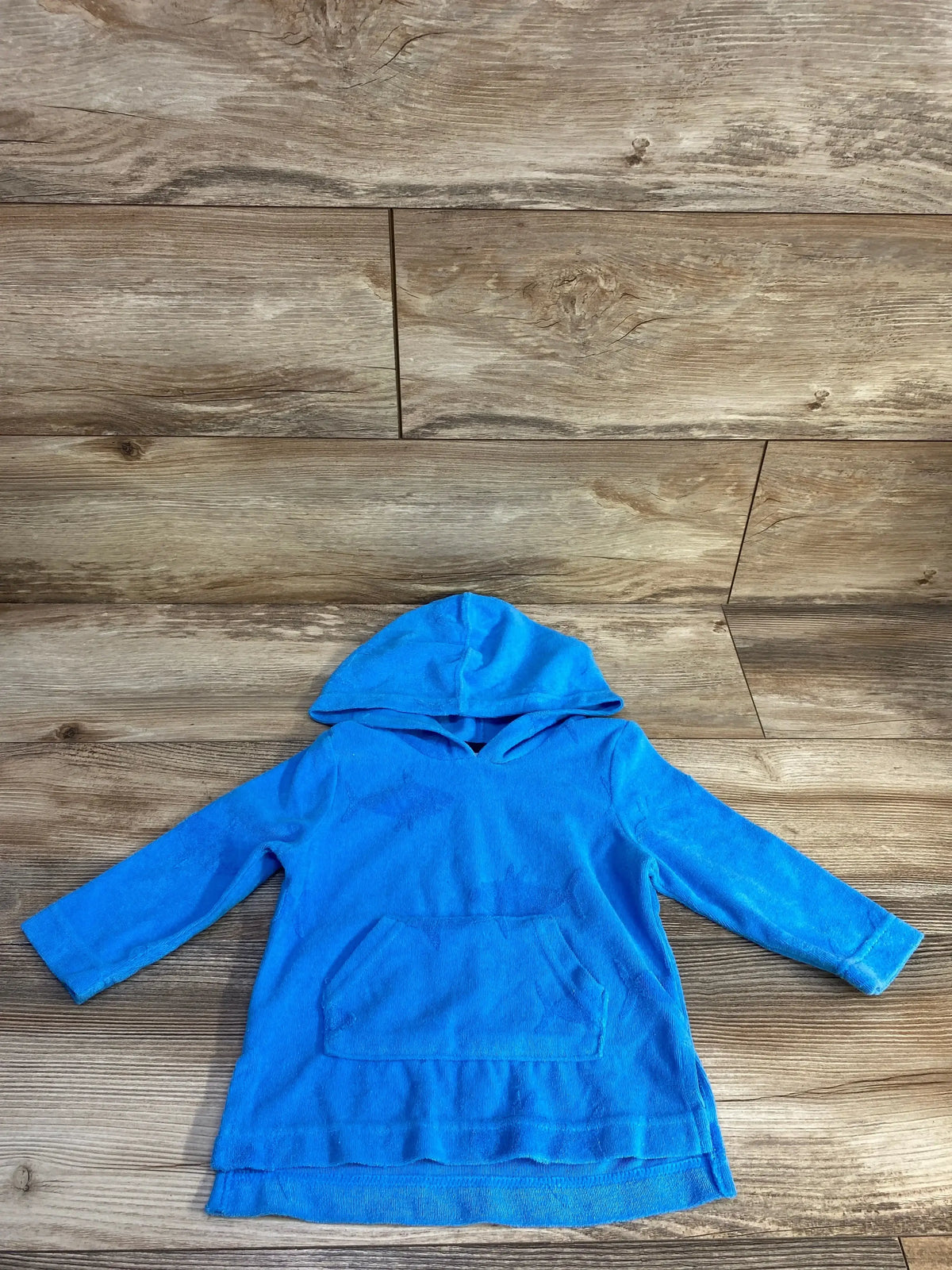 Front flat lay of blue toddler terry cloth hooded swim cover-up showing kangaroo pocket and long sleeves on wood floor