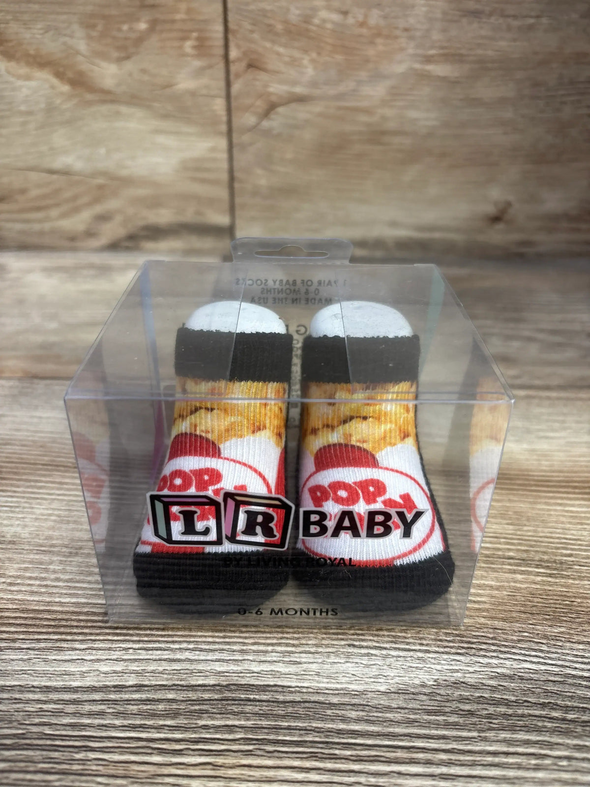 Front view of Living Royal popcorn baby socks showing a popcorn design and 0-6 month size in clear packaging on a wood surface