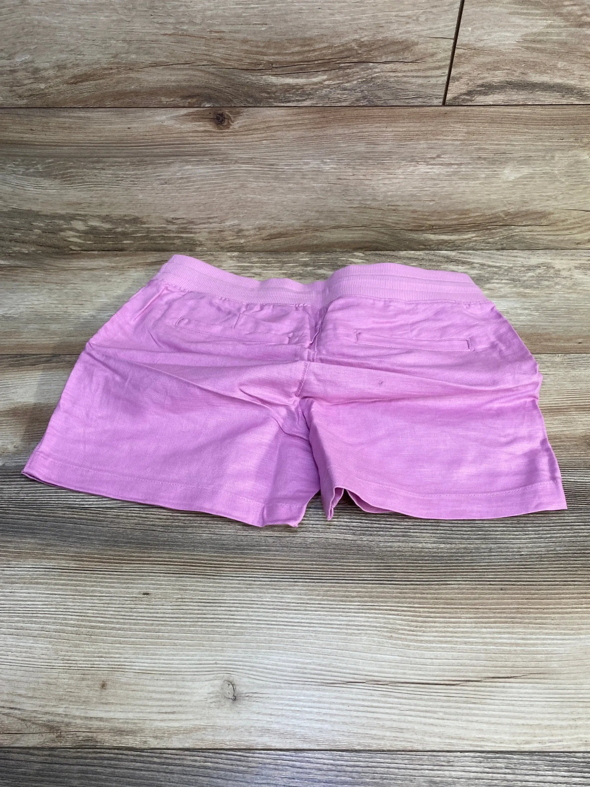 Back view of Gap maternity linen-cotton shorts laid flat showcasing elastic ribbed waistband and back pockets on wood background