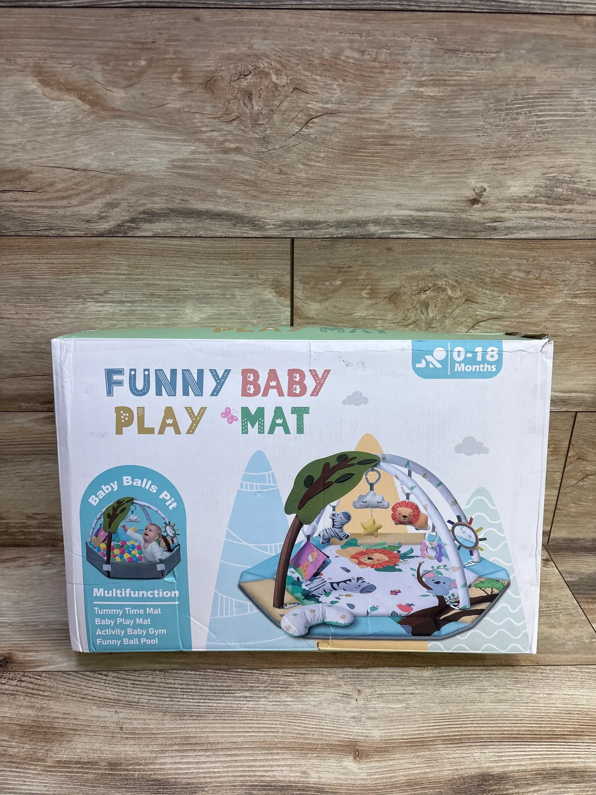 Front view of the NEW Jyusmile 8-in-1 Tummy Time Mat Baby Play Gym box showing arches and toys on a wood floor