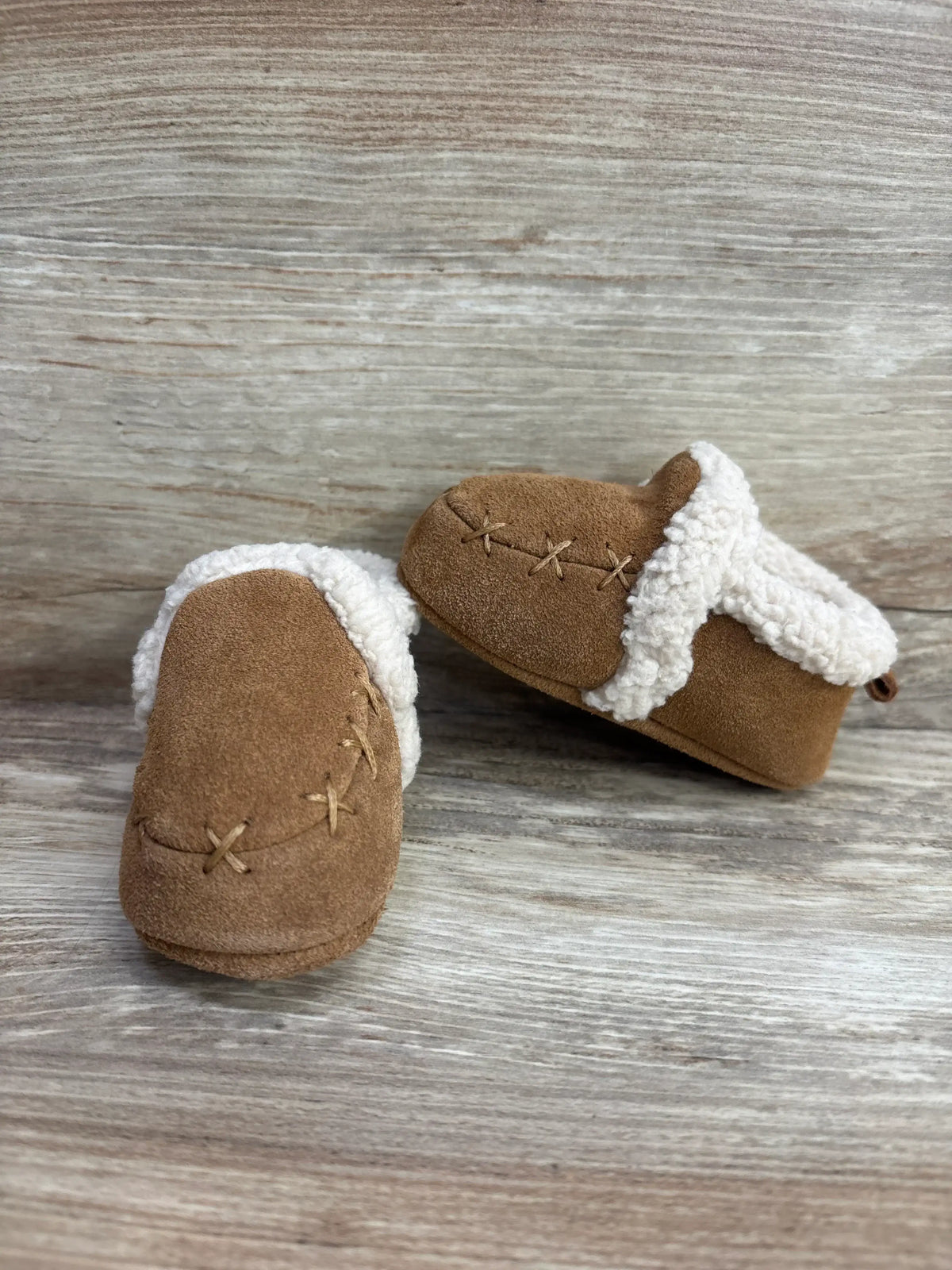 Brown suede baby moccasins with faux fur lining on wood background