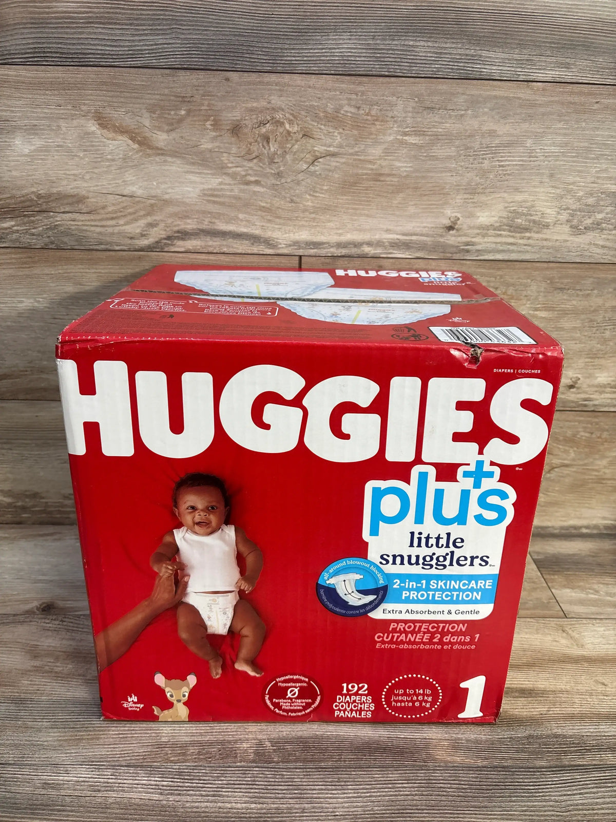 Front view of Huggies Plus Little Snugglers diapers box showcasing 192 diapers, size 1, and 8 to 14 lb fit with wood background
