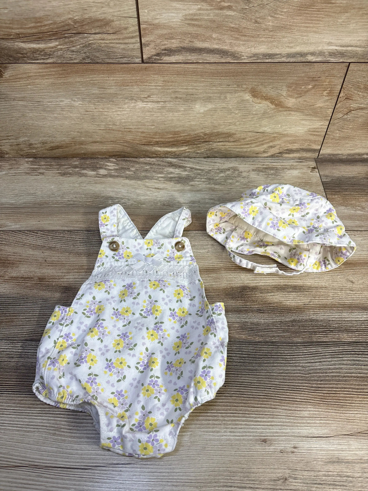 Overhead view of Little Lass floral bubble shortalls and bucket hat set showcasing white floral print on a wood floor