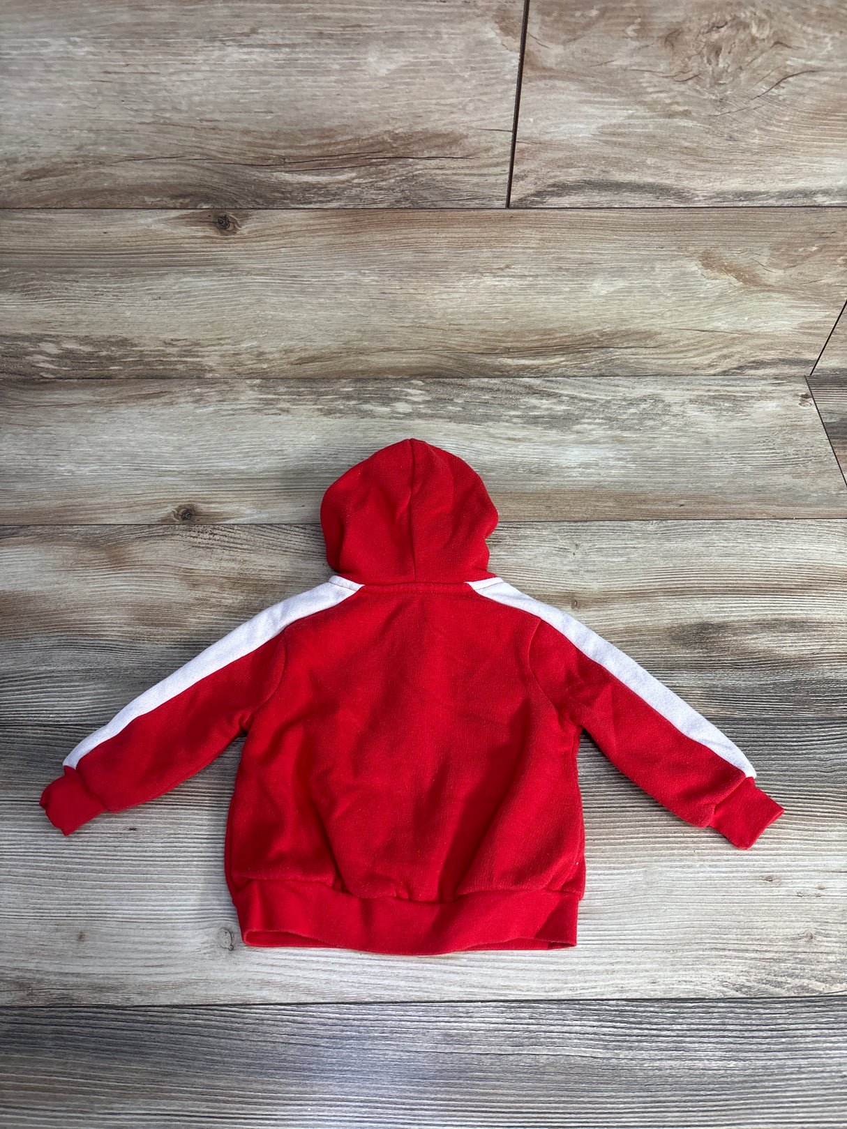 Red hooded sweatshirt with white stripes on sleeves lying flat on wooden floor