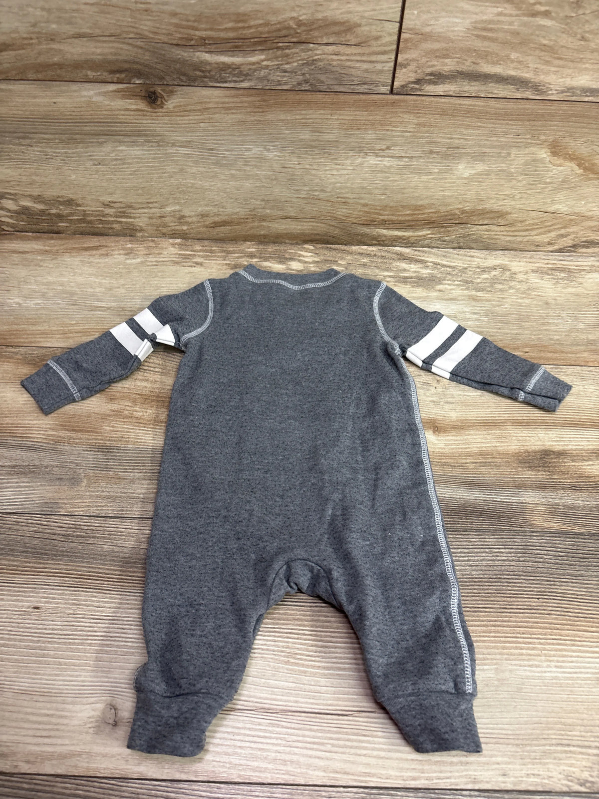 Grey Mini Heroes baby coverall size 6m with white sleeve stripes on a wood background