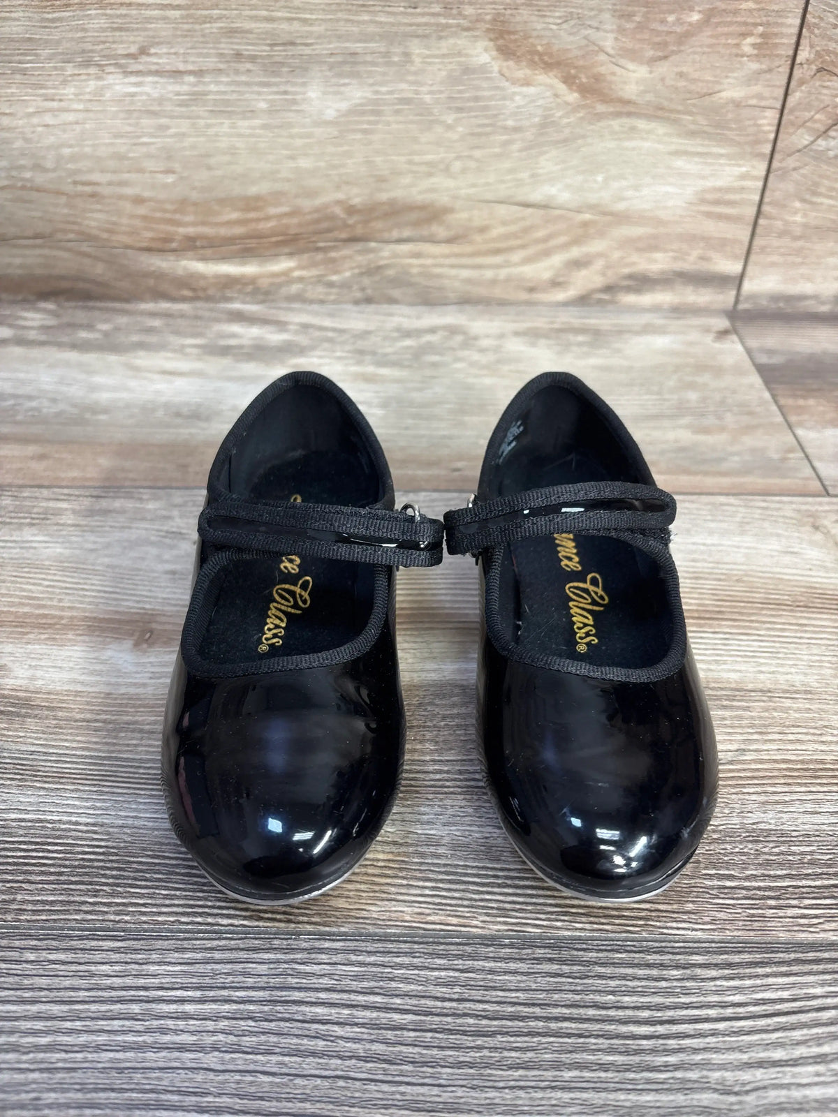Front view of black Dance Class tap shoes in size 10.5C showcasing glossy uppers and double straps on a wood-grain floor