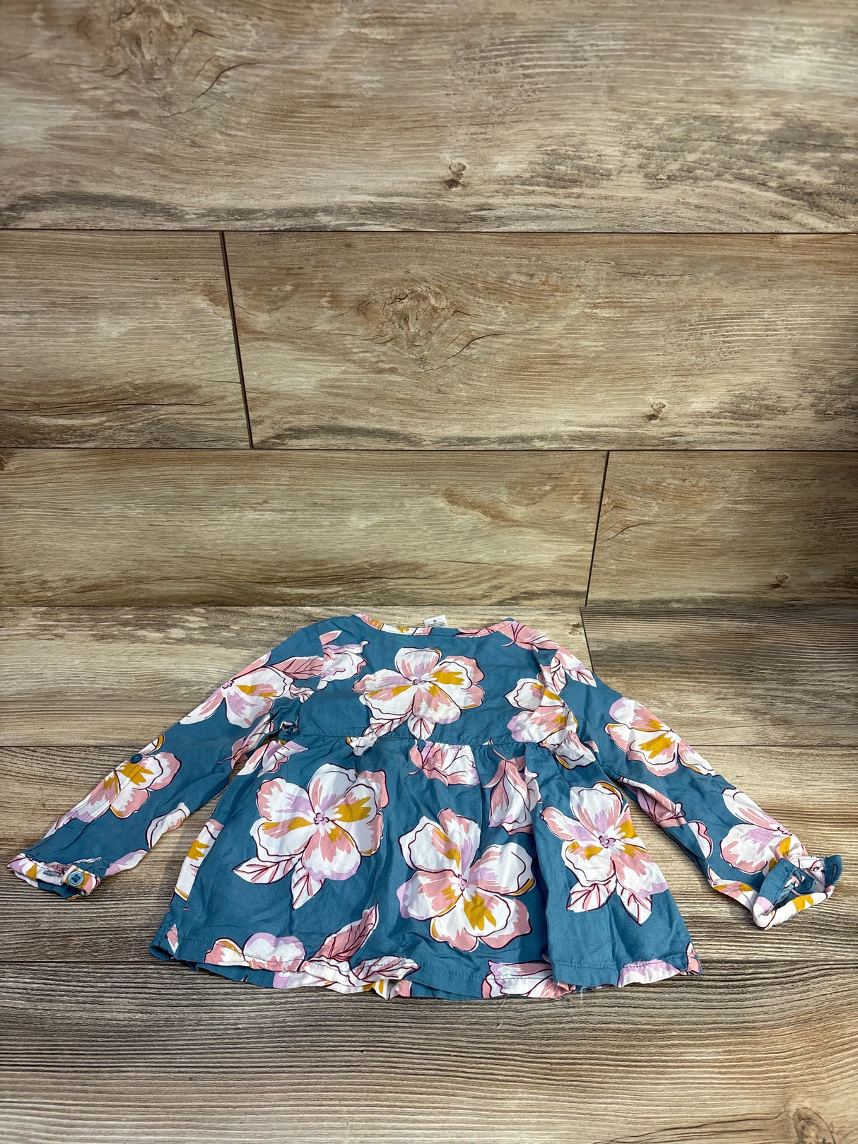 Front flat lay of Carter’s blue viscose button front top with large pink floral print and button cuffs on wood background