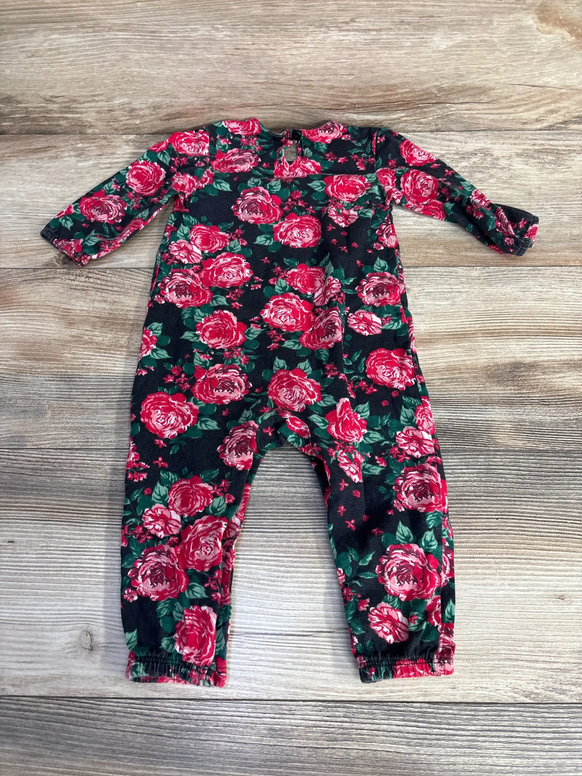 Flat lay of baby floral coverall showcasing red rose print, long sleeves, and elastic ankle cuffs on a light wood background