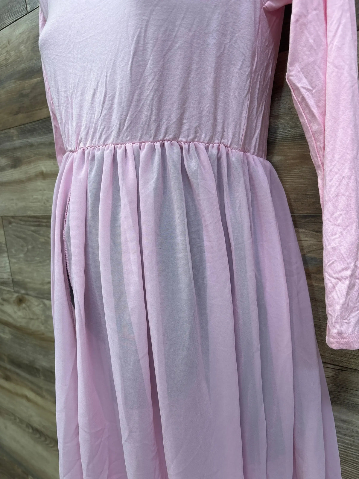 Front close-up of pink maternity maxi dress showing long sleeve, gathered empire waist and sheer skirt on wood background