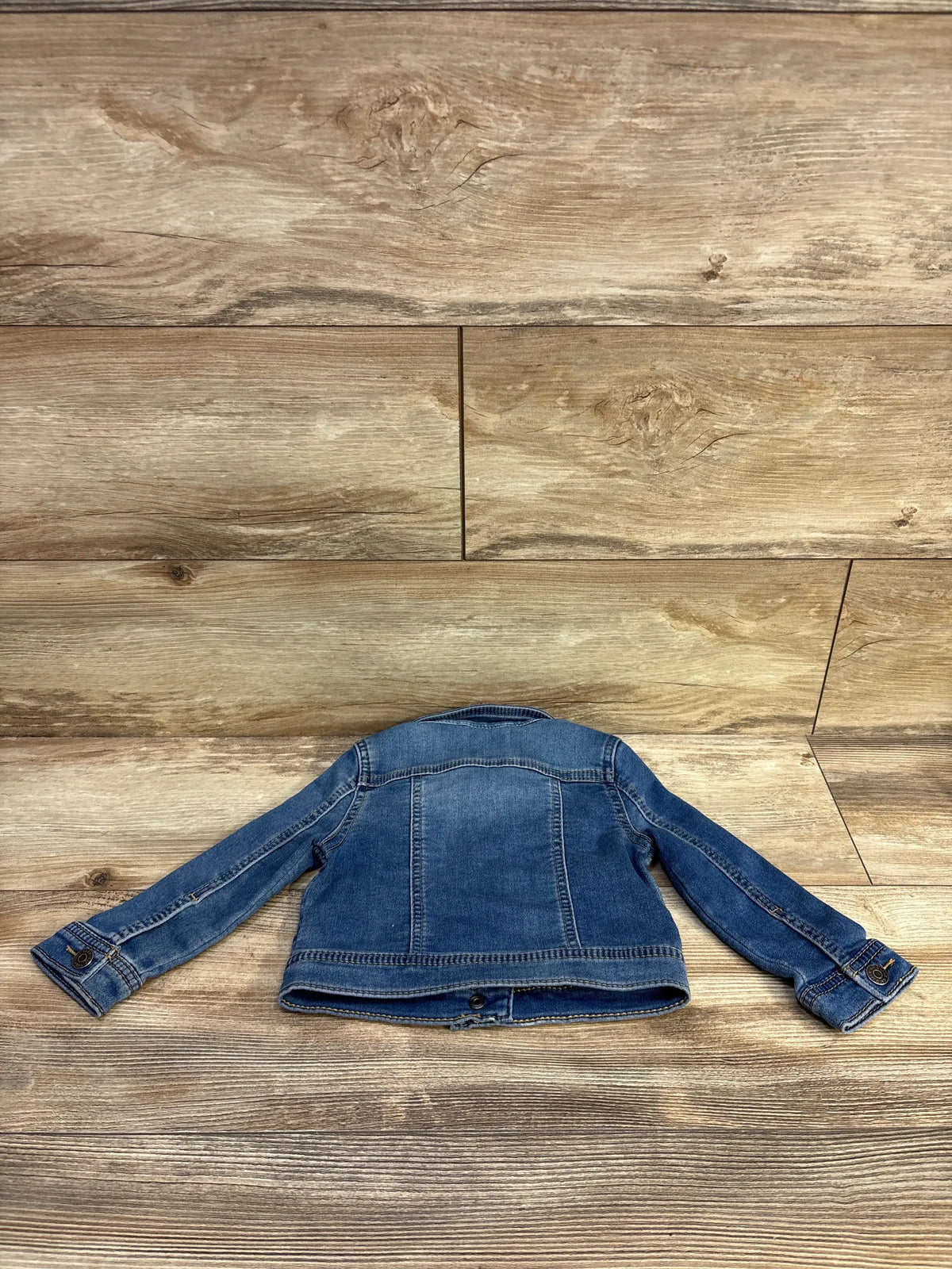 Back view of Cat & Jack blue denim jacket in size 18M showcasing long sleeves and button cuffs on a wood-look floor