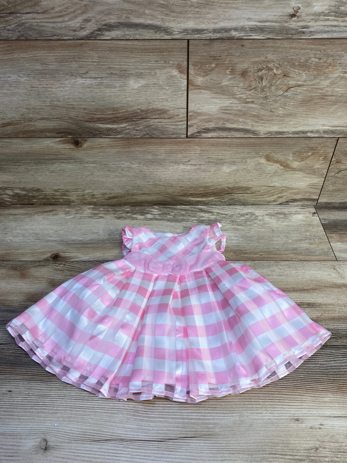 Front flat lay of pink and white gingham baby dress with rosette waist, ruffled sleeves and gathered skirt on wood background