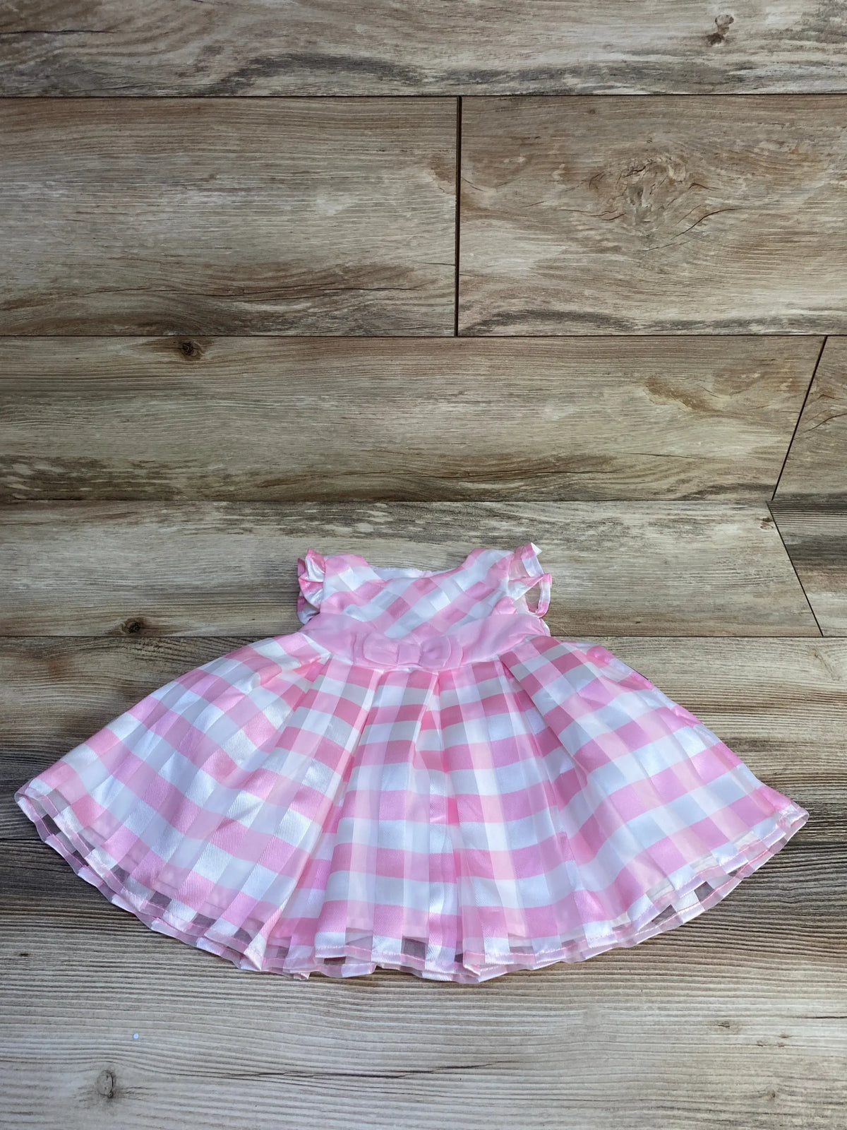 Front flat lay of pink and white gingham baby dress with rosette waist, ruffled sleeves and gathered skirt on wood background
