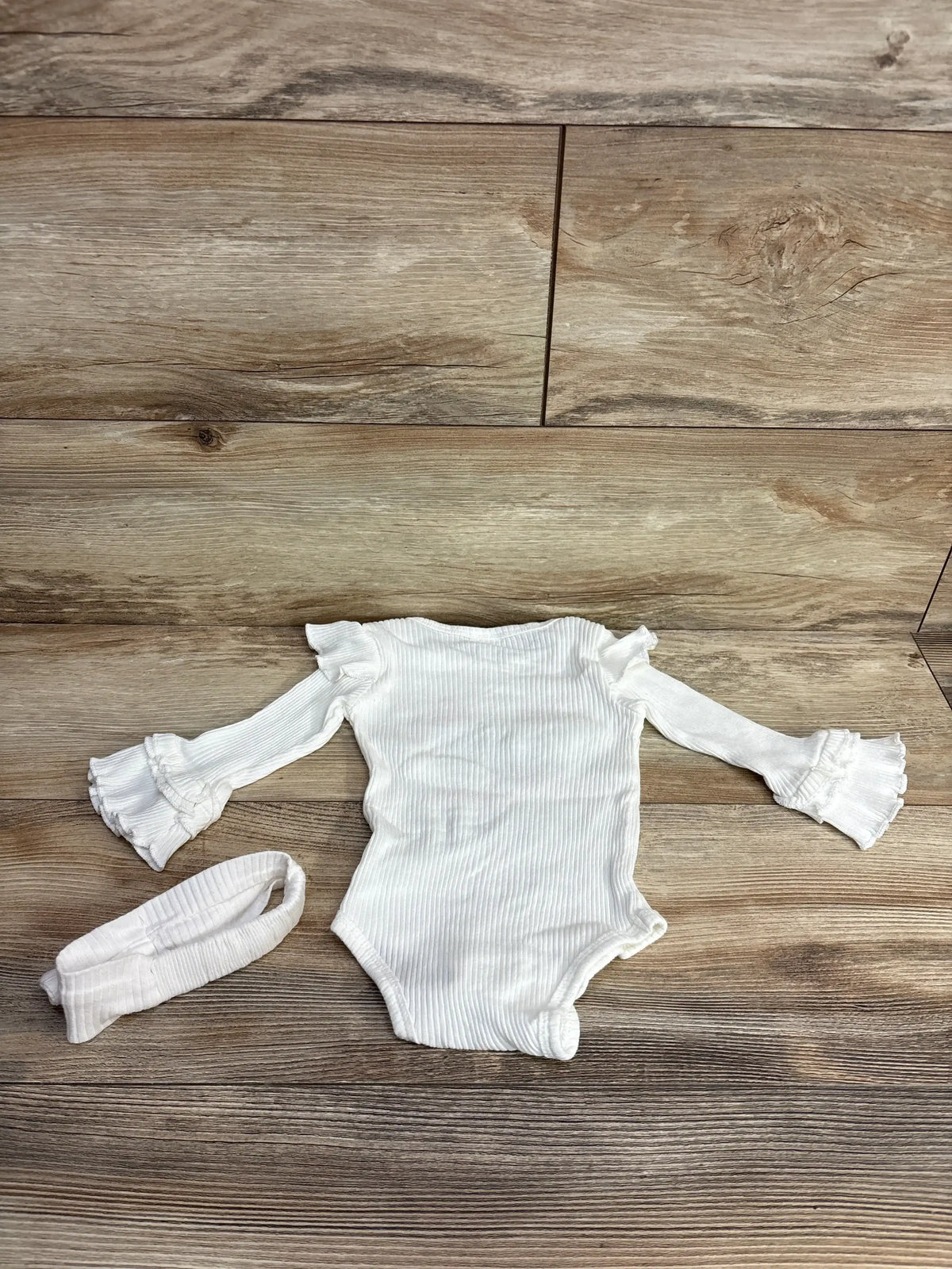 White ribbed baby onesie with ruffled sleeves and matching headband on wood floor