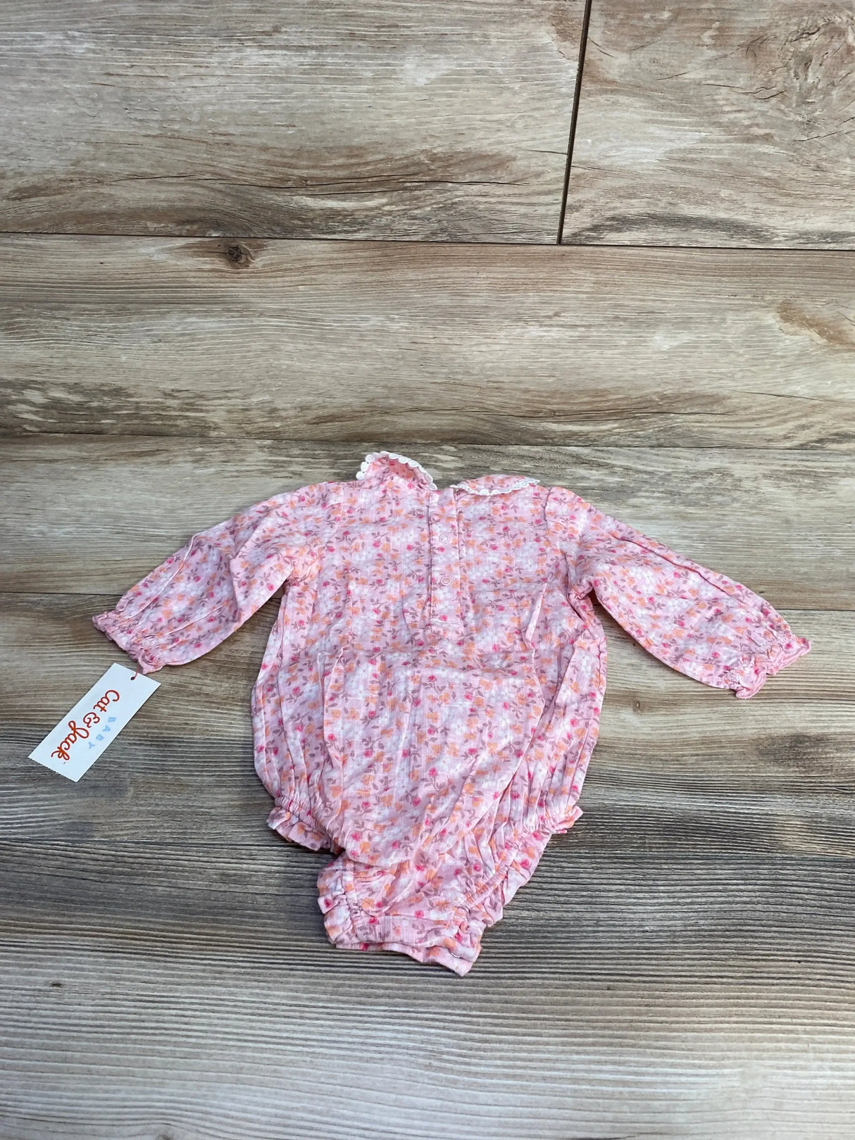 Flat lay of Cat & Jack pink floral baby romper with ruffled collar and elastic leg openings on wood background