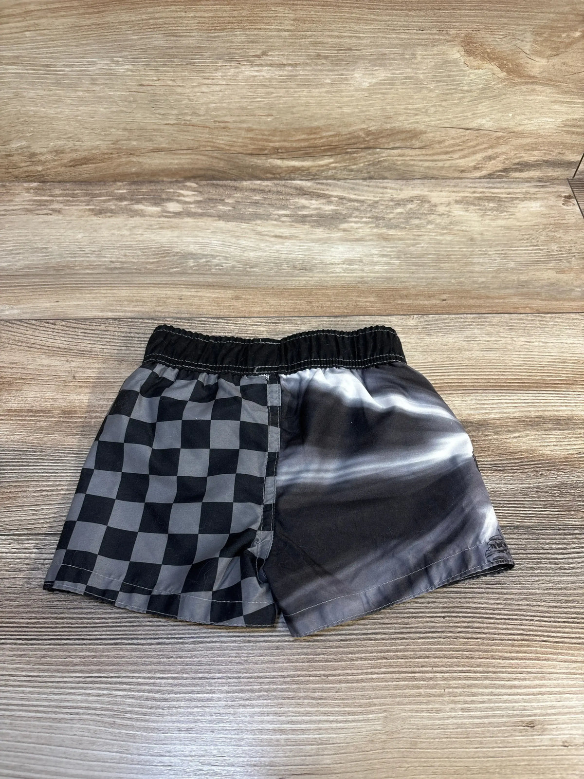 Kids black shorts with checkerboard and tie-dye pattern, elastic waistband, on wood background