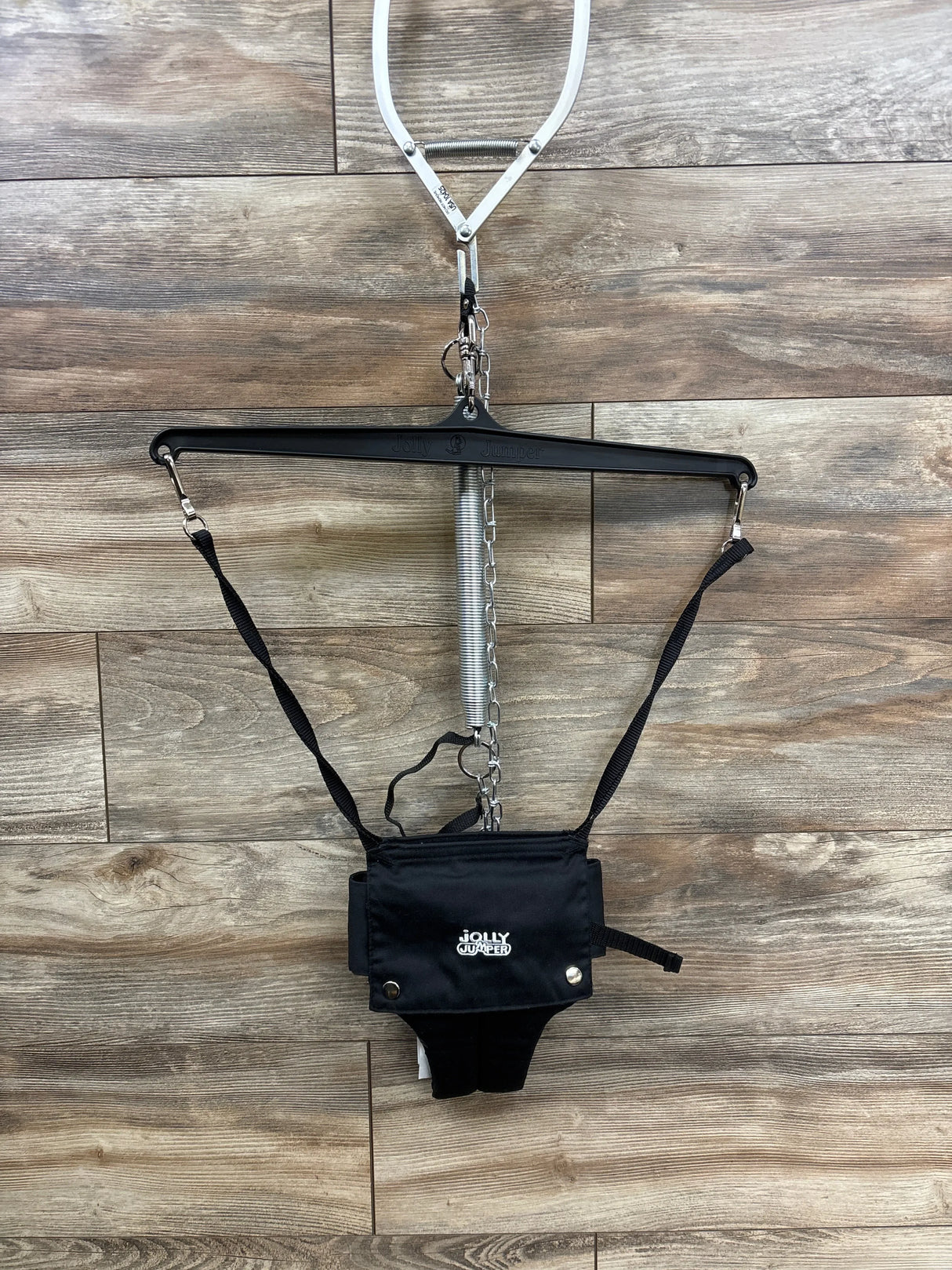 Front view of Jolly Jumper baby jumper with door clamp in black showing harness seat spring and clamp on wood plank floor