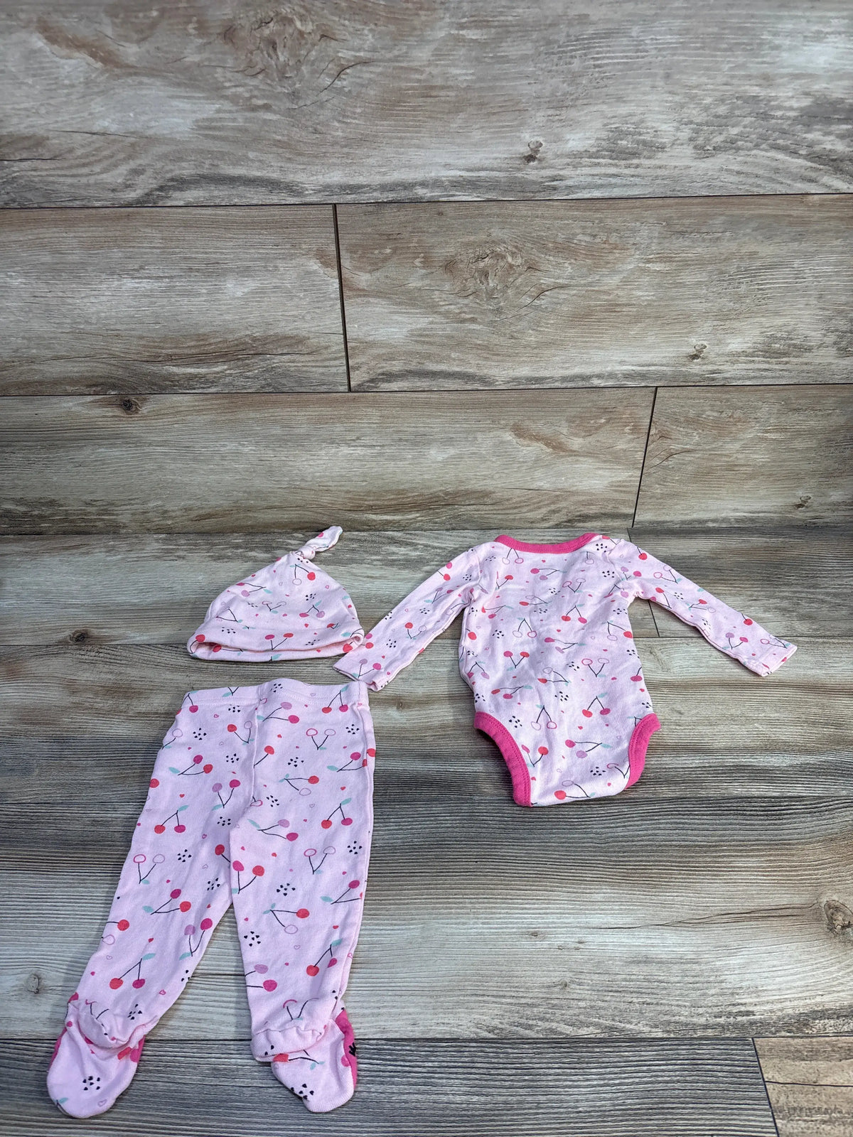 Overhead view of Koala Baby 3pc Kimono Shirt Set showing pink bodysuit, footed pants, and knot hat on a wood-look floor
