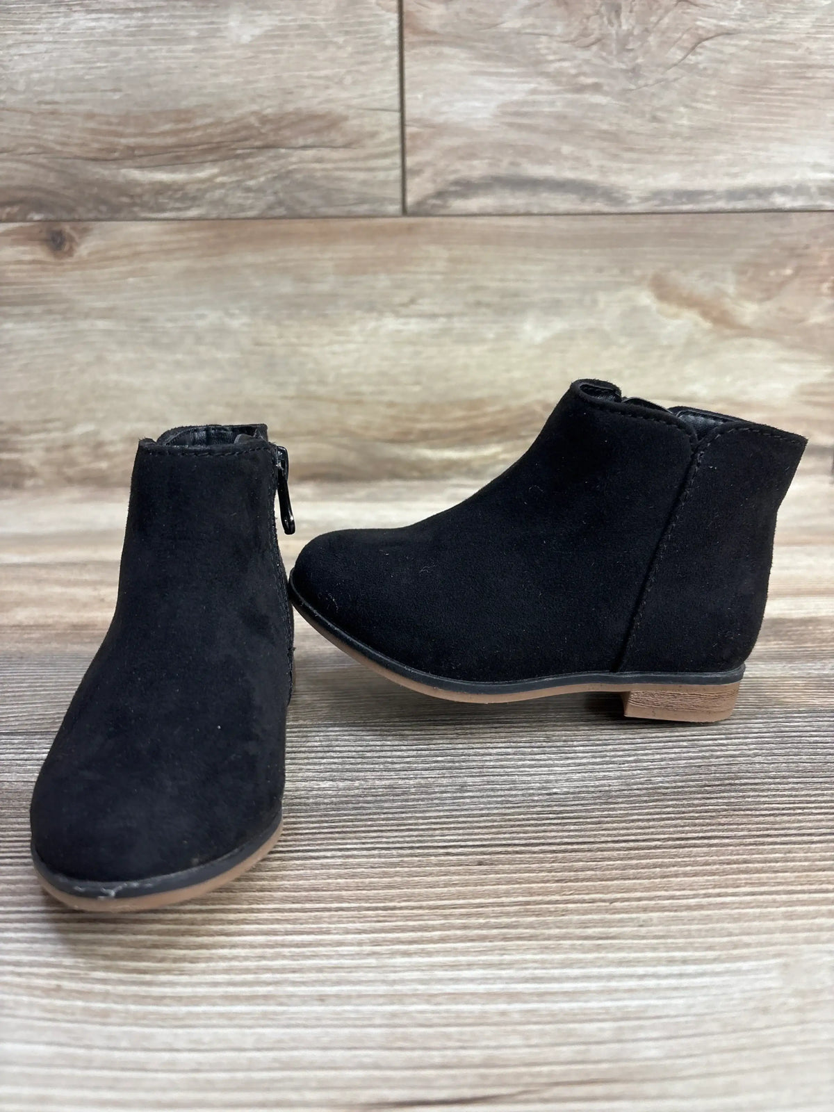 Pair of black suede toddler ankle boots with side zipper on wood background