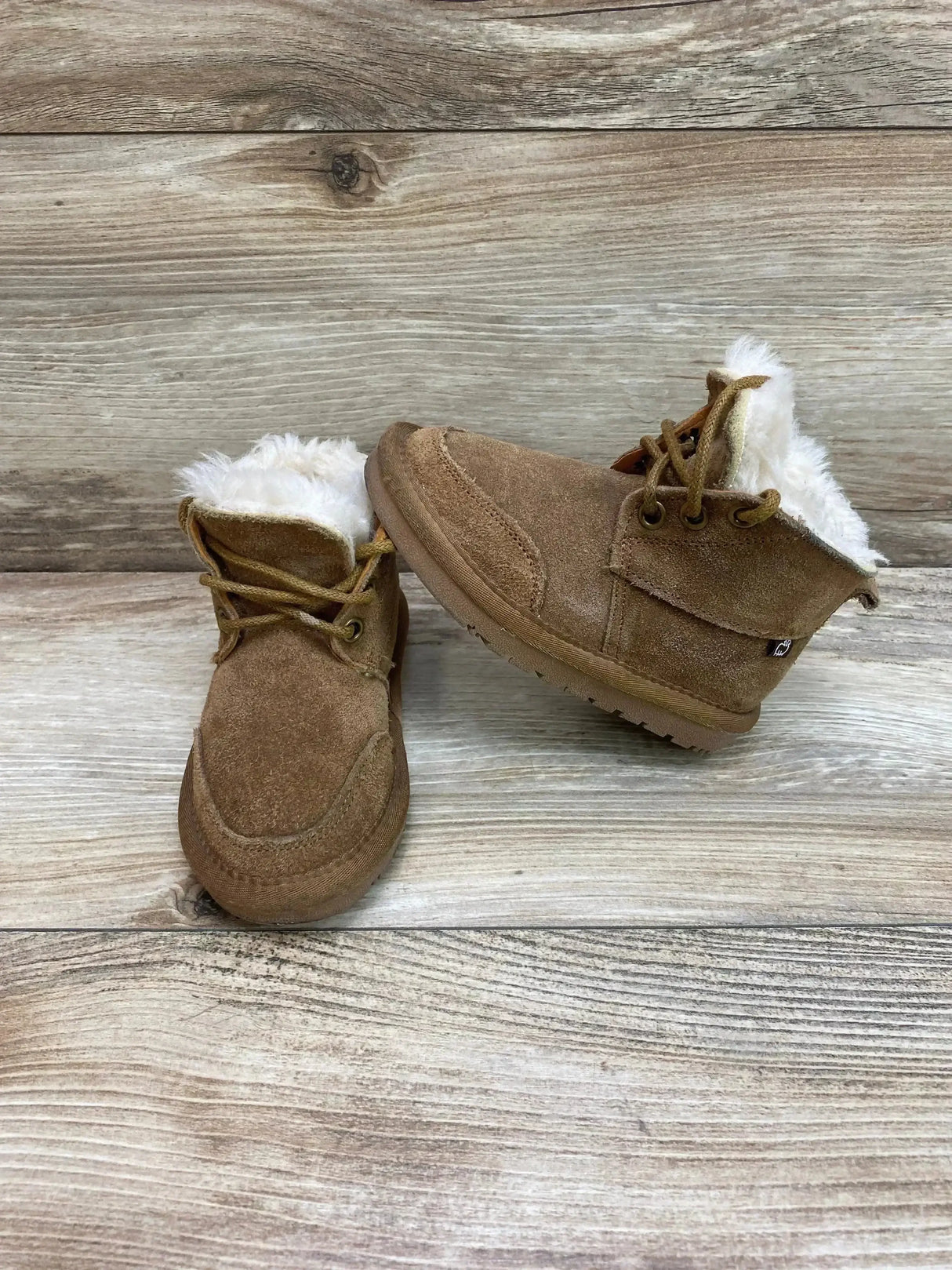 Front three quarter view of chestnut Lamo chukka suede toddler boots showing white faux fur lining and laces on light wood background