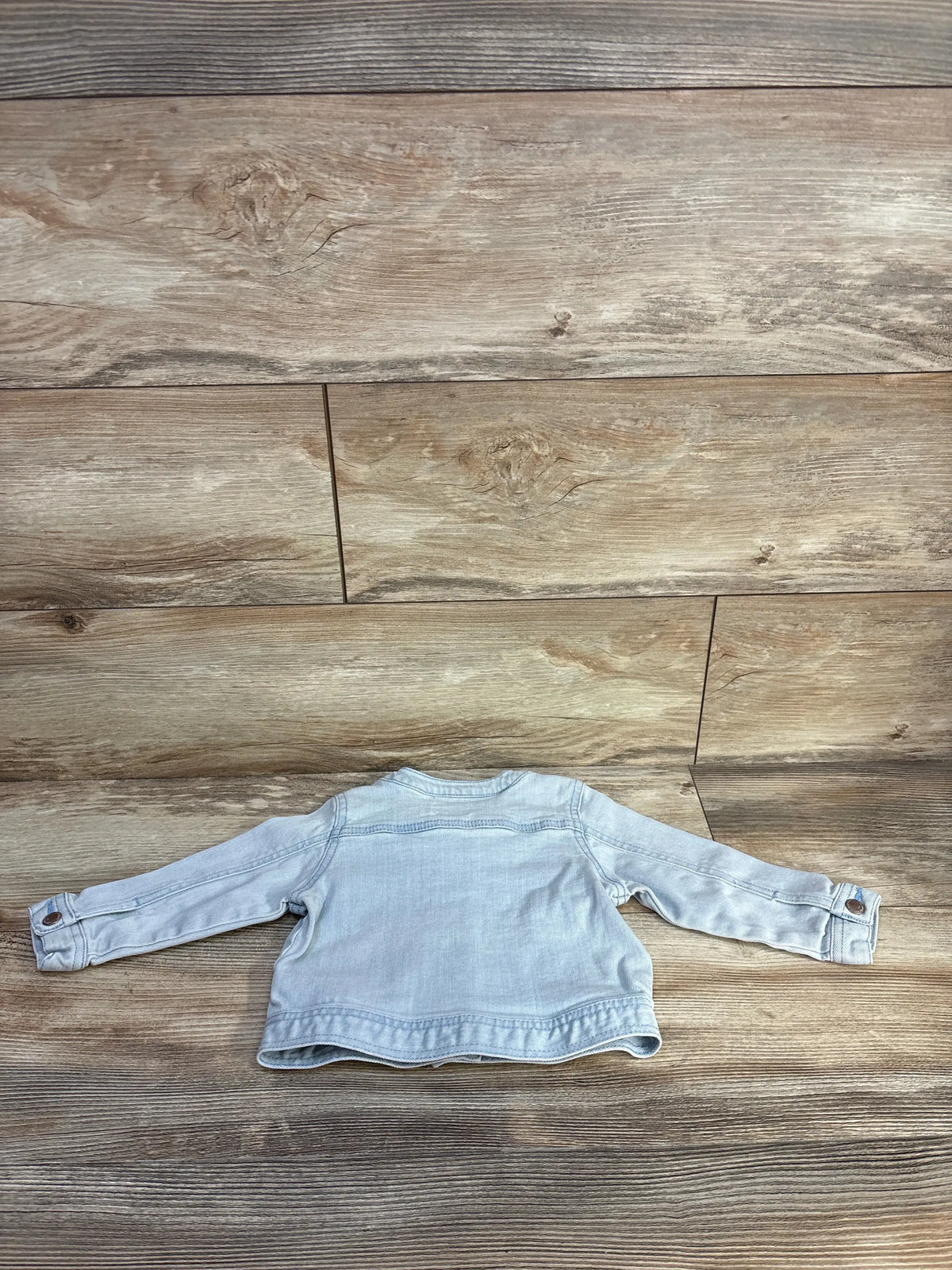 Back view of Old Navy blue denim jacket showcasing long sleeves and button cuffs on a wood-look background