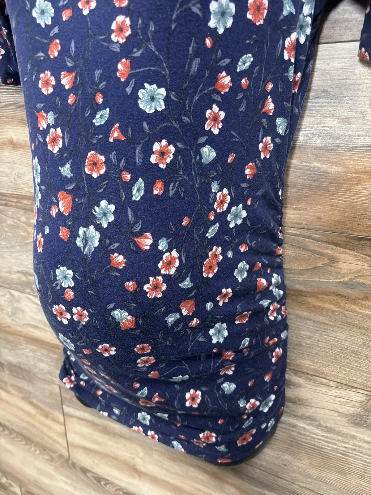 Close-up of navy maternity ruched shirt showcasing red and teal floral print and side ruching against wood floor background
