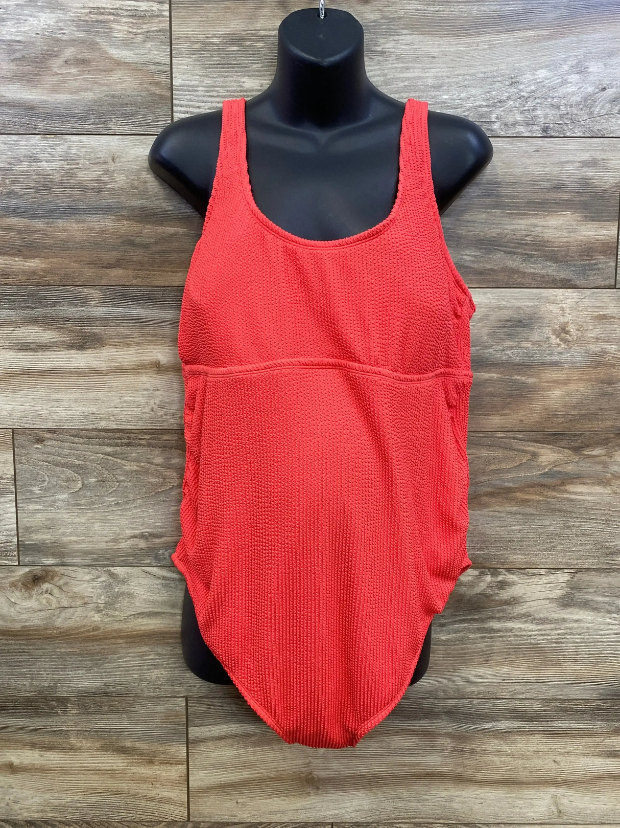 Front view of red maternity one-piece swimsuit with scoop neckline, tank straps, textured fabric and empire seam on wood