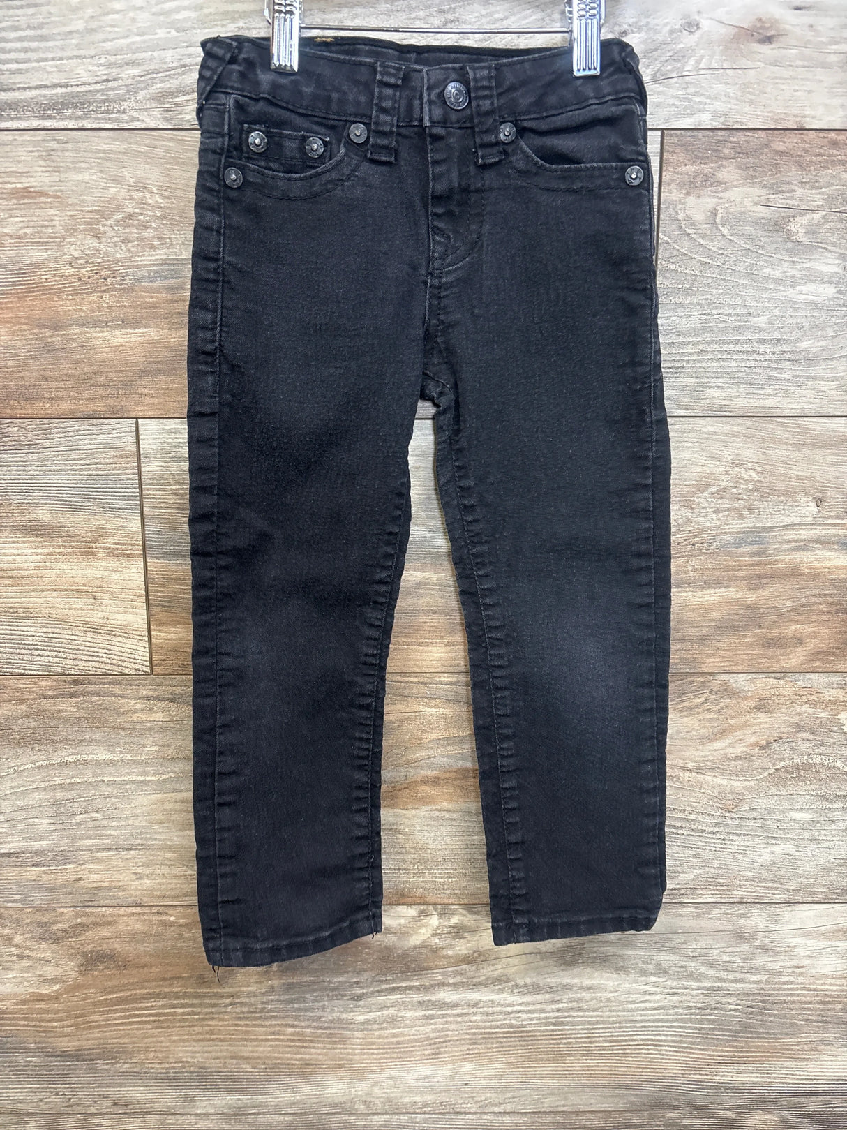 Black denim kids jeans with front pockets and belt loops on wood background