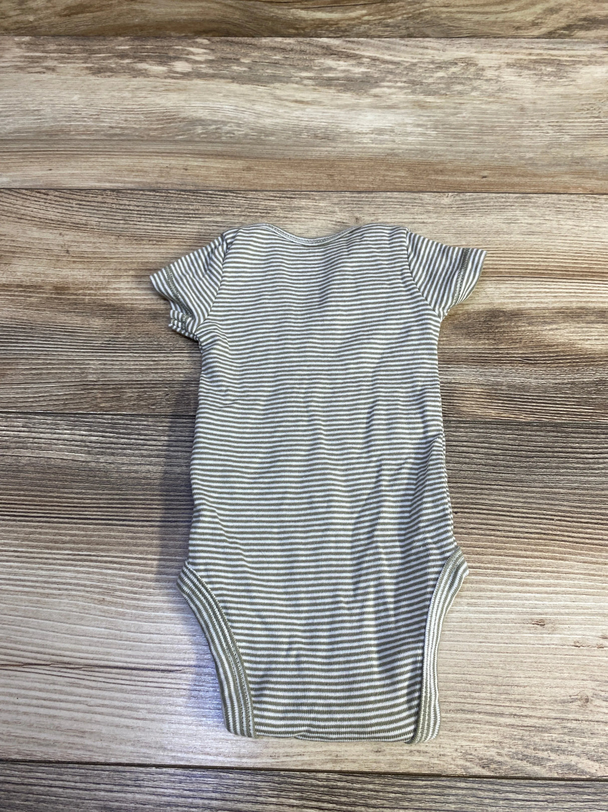 Flat lay of Carter’s newborn bodysuit showing thin green-and-white stripes, short sleeves, and ribbed leg openings on wood