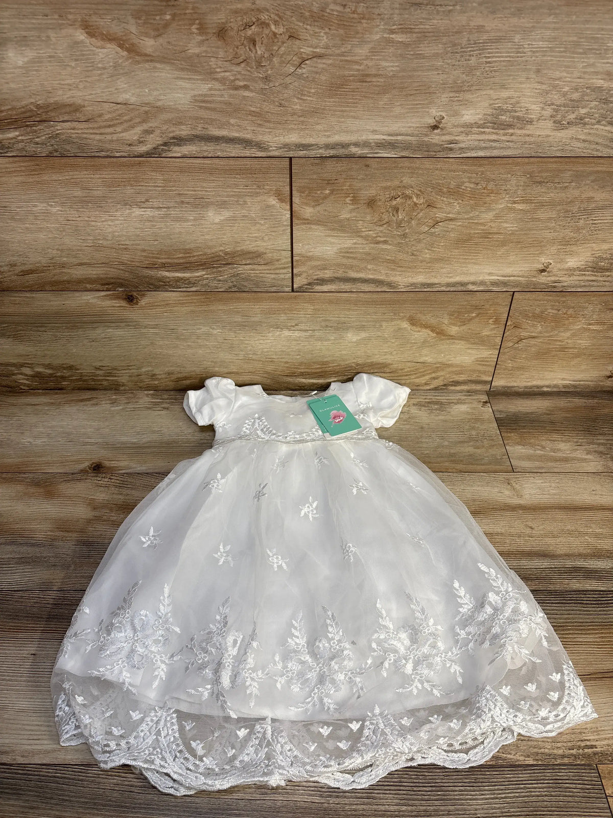 Front view of white Glamulice christening dress in size 3m showcasing floral embroidery and cap sleeves on a wood floor