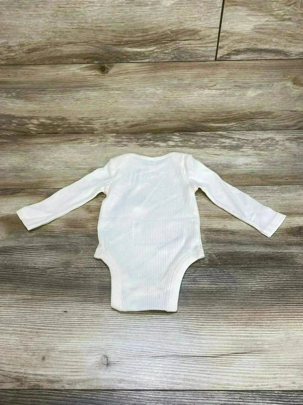 Top-down view of Old Navy ivory rib-knit baby bodysuit 3-6m showing long sleeves and ribbed texture on light wood background