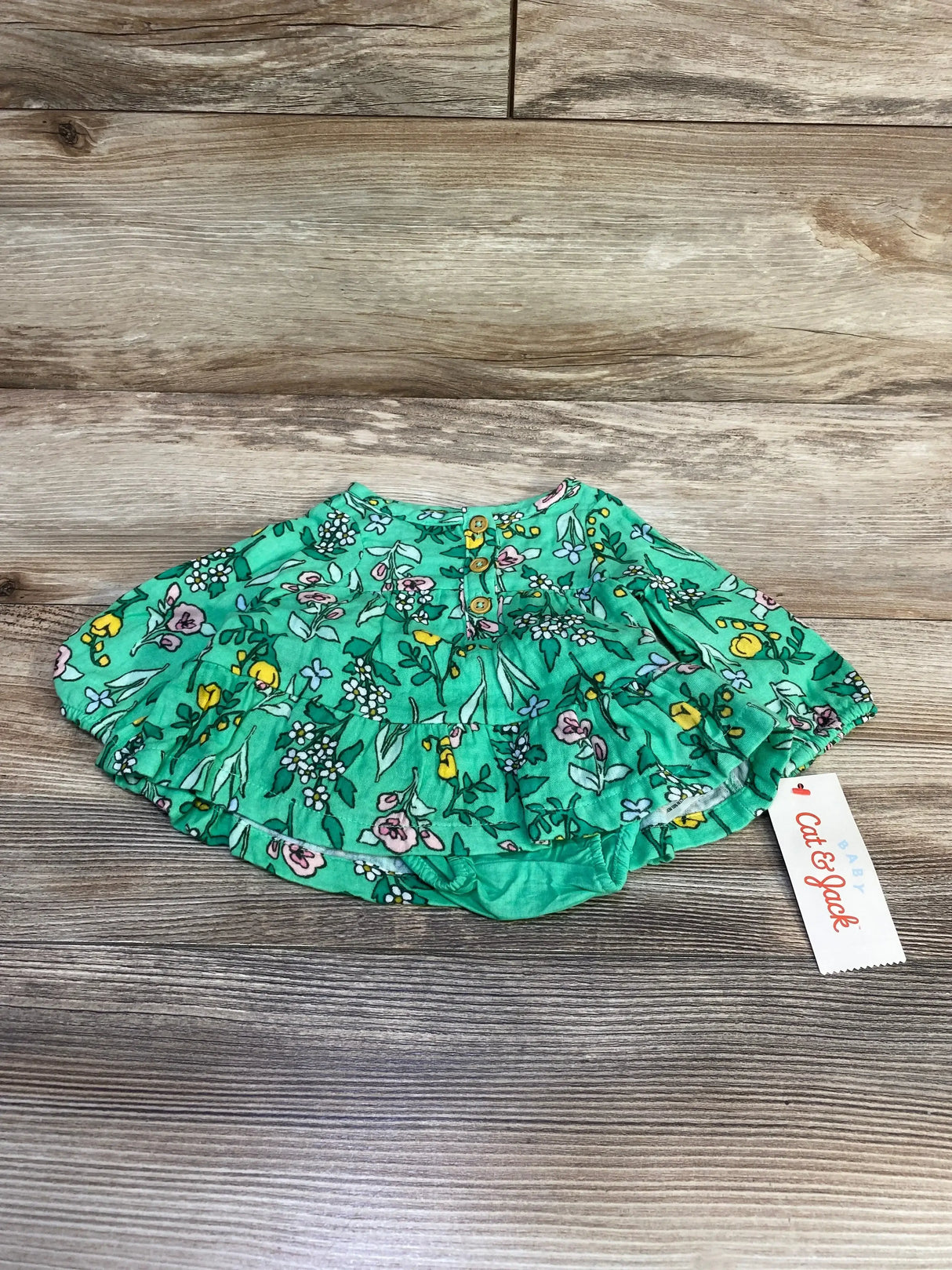 Flat lay of Cat & Jack newborn floral henley dress and bloomers showing green print, wooden buttons on wood background