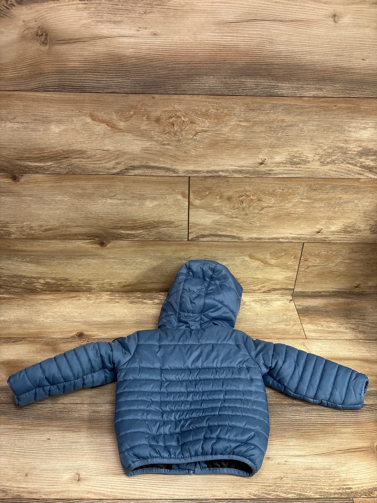 Back view of a blue Nike puffer zip jacket for toddlers, size 18m, on a wooden background.