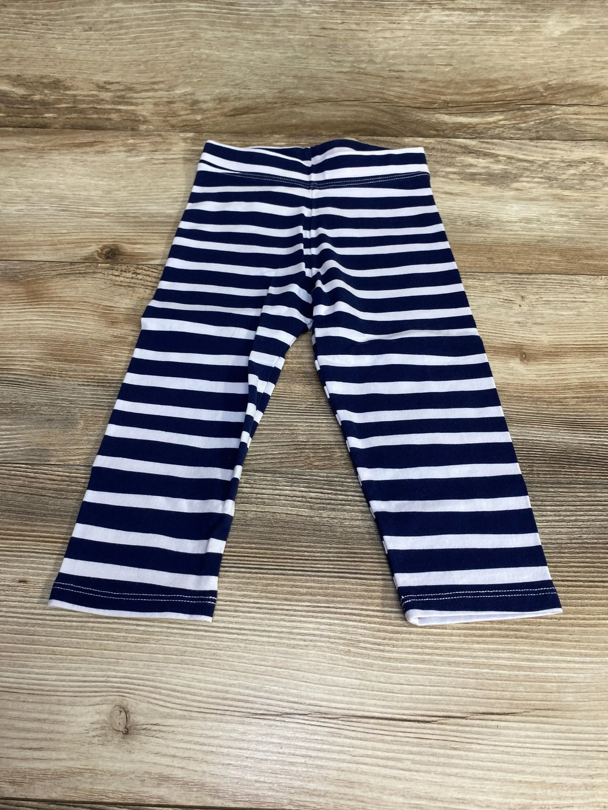 Flat lay of navy and white striped toddler leggings showing front full-length and elastic waistband on wood background