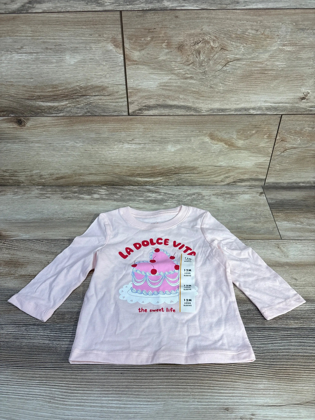 Flat lay of Cat and Jack pink long-sleeve shirt with cake graphic reading La Dolce Vita, the sweet life on wood background