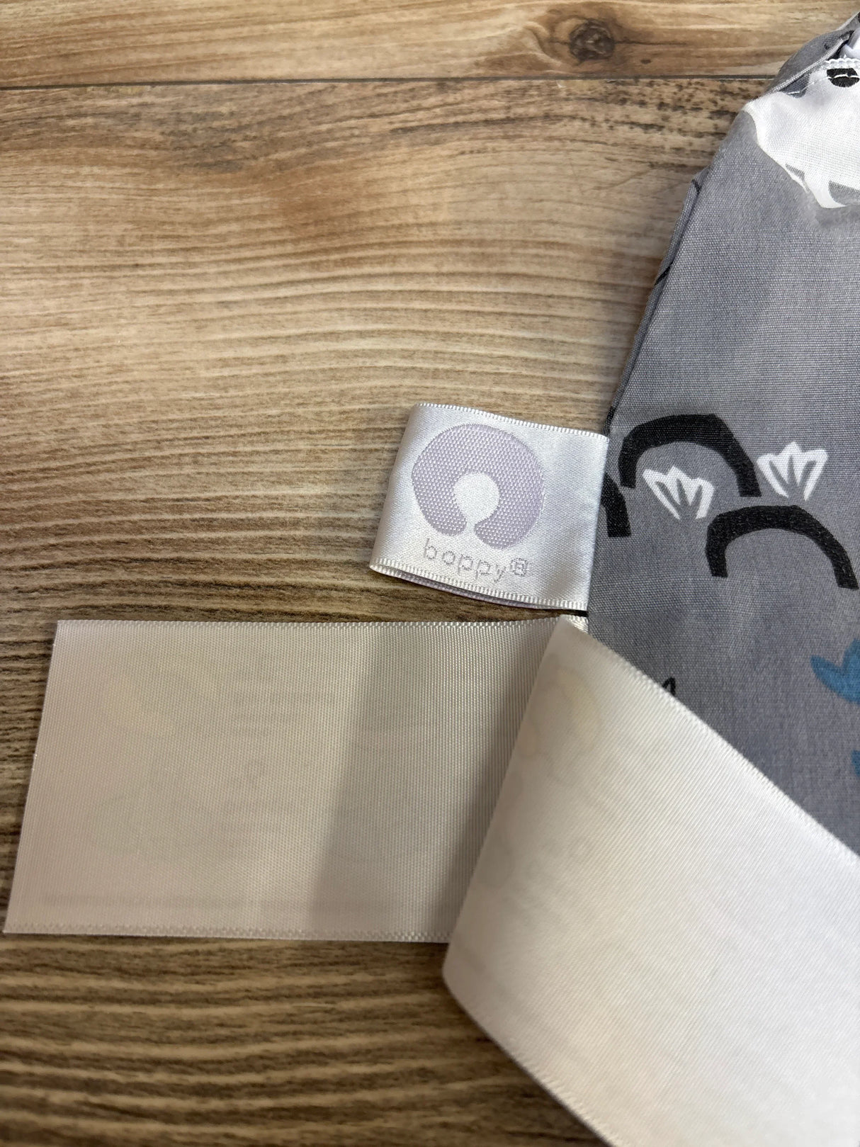 Close-up of Boppy Nursing Pillow Cover Grey Dinosaur Print showcasing fabric label and white Velcro strap on wood background