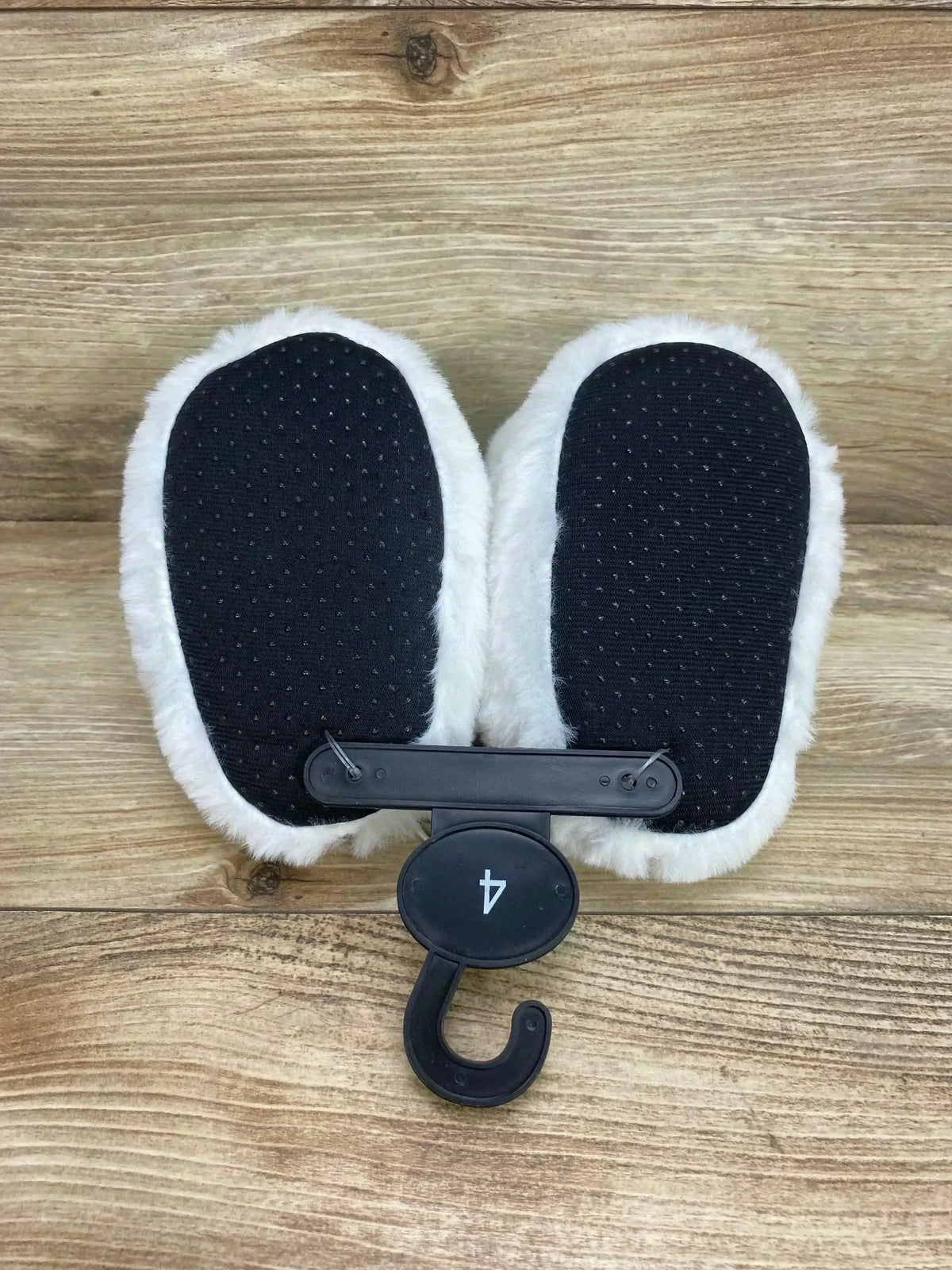 Top view of Abominable Snowman Bumble slippers size 4C showing black non slip soles and white plush fur on wood background