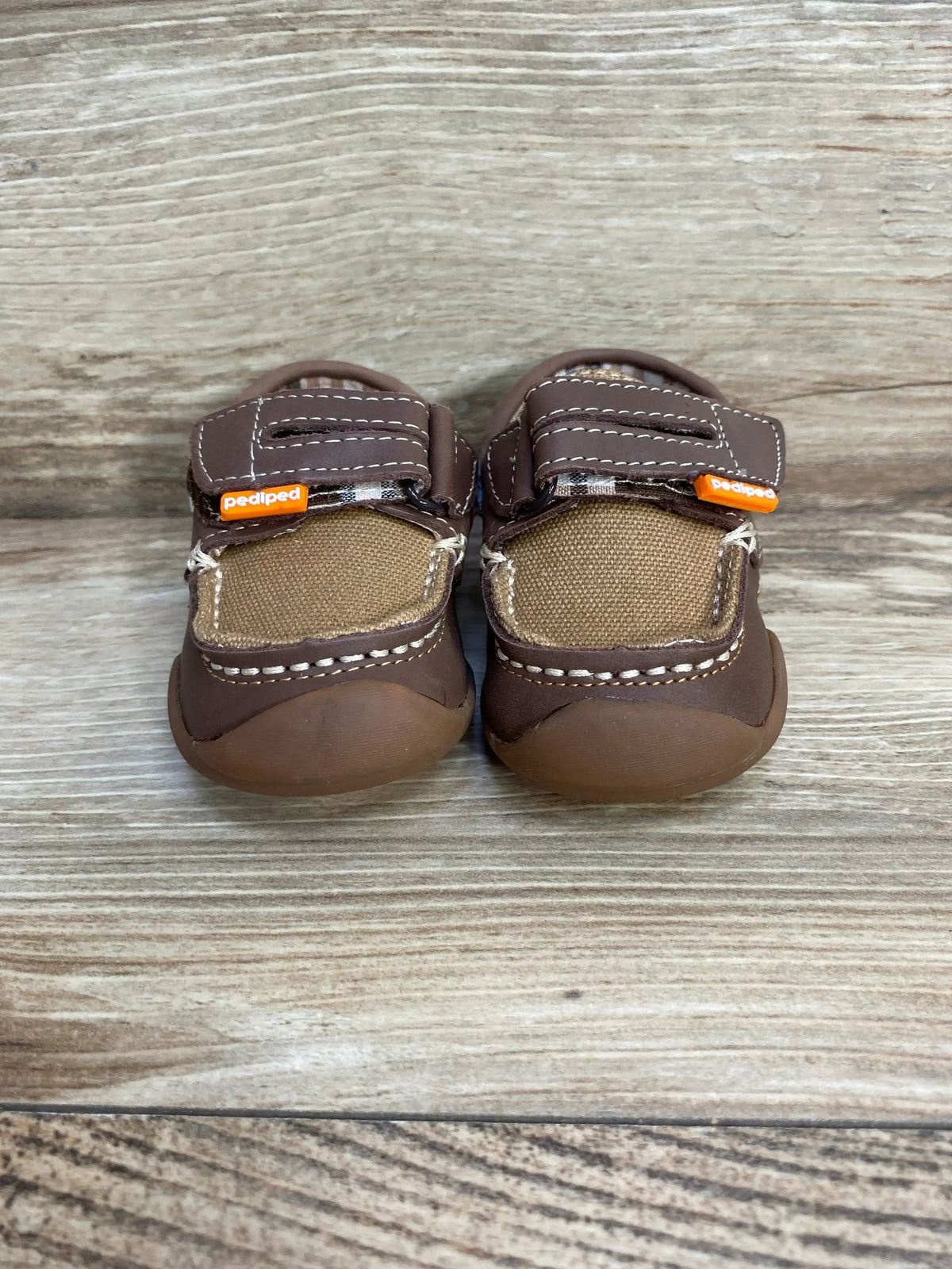 Front view of brown Pediped Grip-N-Go Naples toddler loafers with Velcro straps and rubber toe caps on wood background