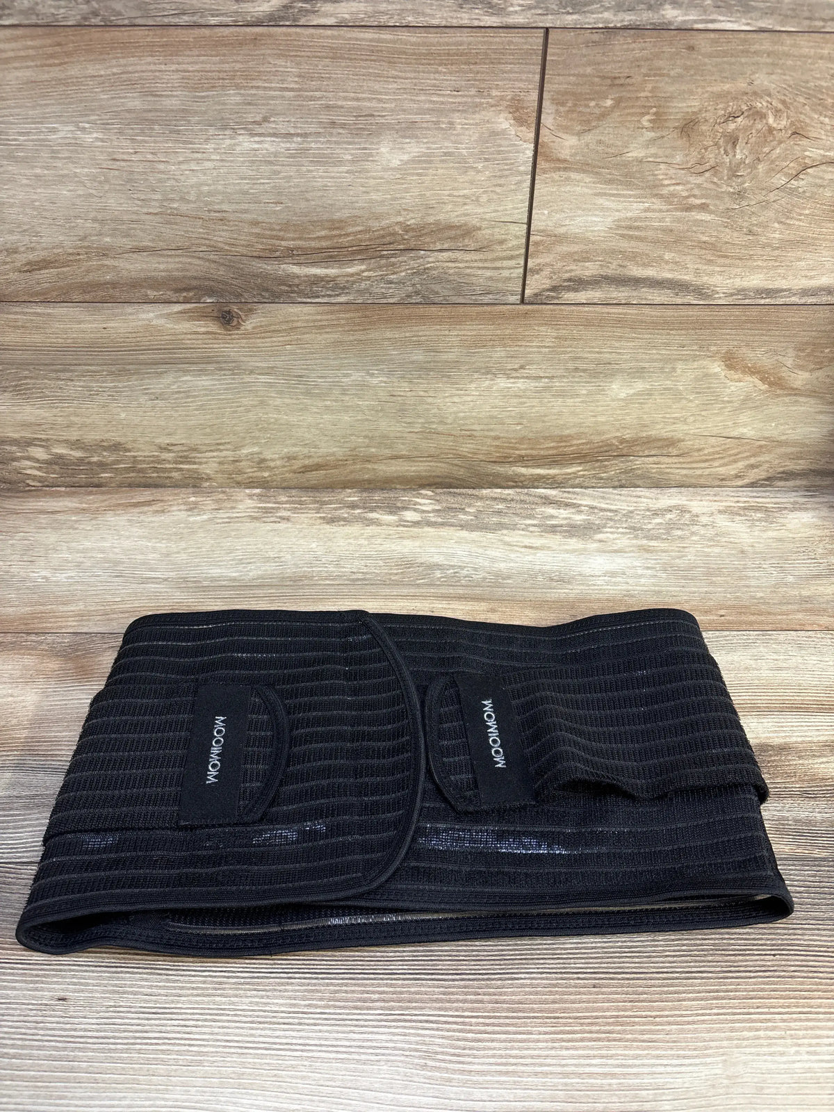 Front view of MooiMom bamboo postpartum belly band in black, showcasing ribbed fabric and adjustable wrap closures on a wood floor