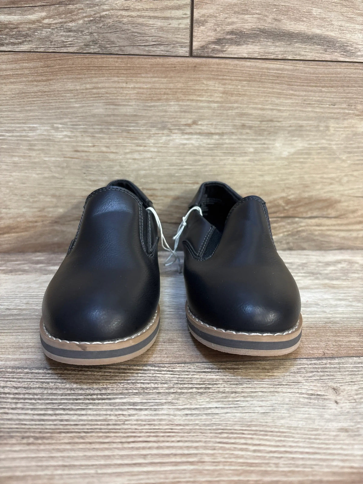 Black kids leather slip-on shoes with tan soles on wooden floor