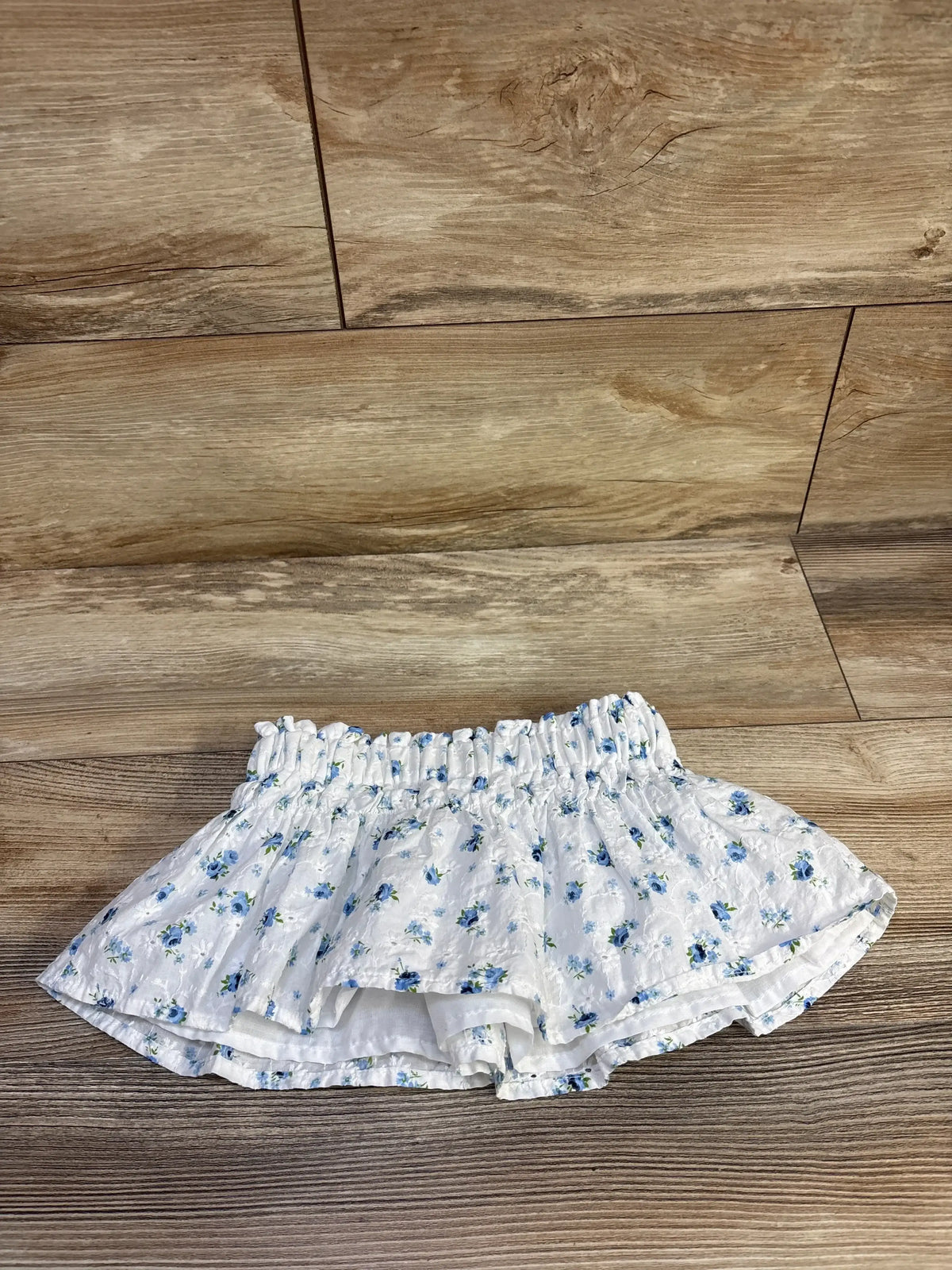 Top-down view of Copper Key white eyelet toddler skirt (2T) showcasing elastic ruched waistband and blue floral print on wood background