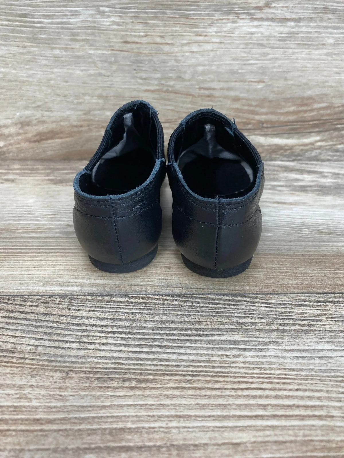 Rear view of Capezio black jazz slip-on shoes size 10C showing heel seam and low-profile soles on wood background