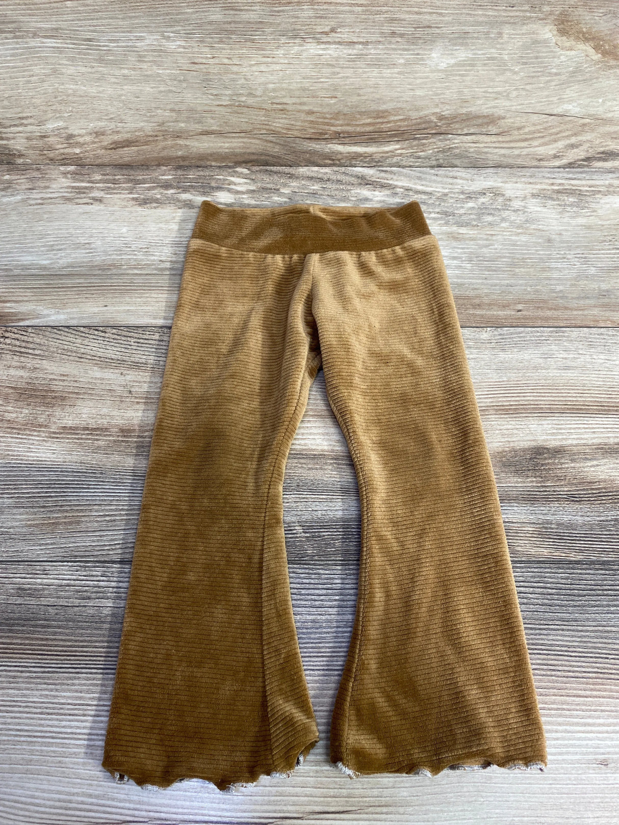 Brown ribbed velvet toddler pants with scalloped hems on wood background