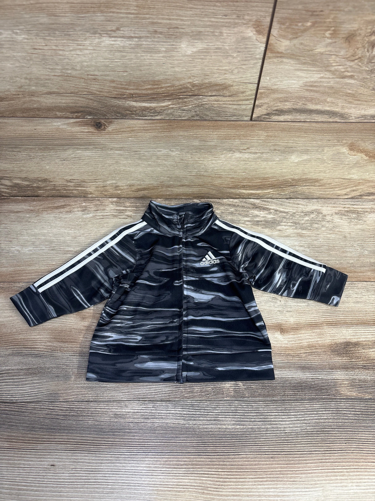 Black and gray Adidas track jacket with white stripes on wooden floor