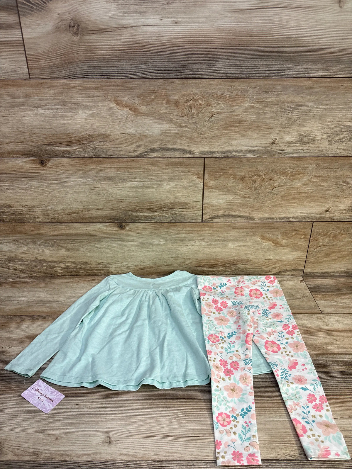 Flat lay of Tommy Bahama two-piece set showcasing aqua embroidered long-sleeve top and floral leggings on wood backdrop