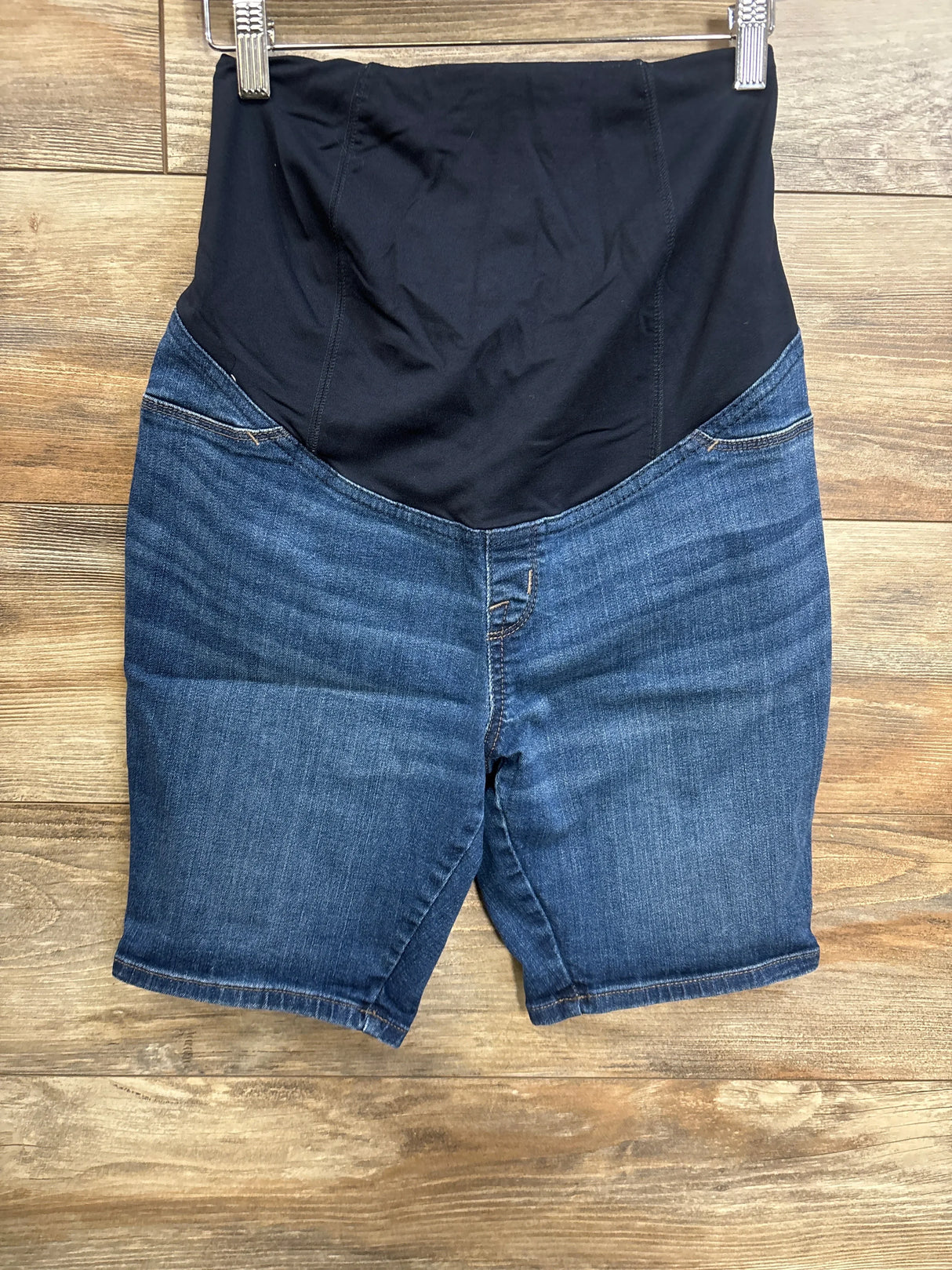 Front view of maternity Bermuda shorts showcasing full black belly support panel and blue denim knee-length legs on wooden floor background