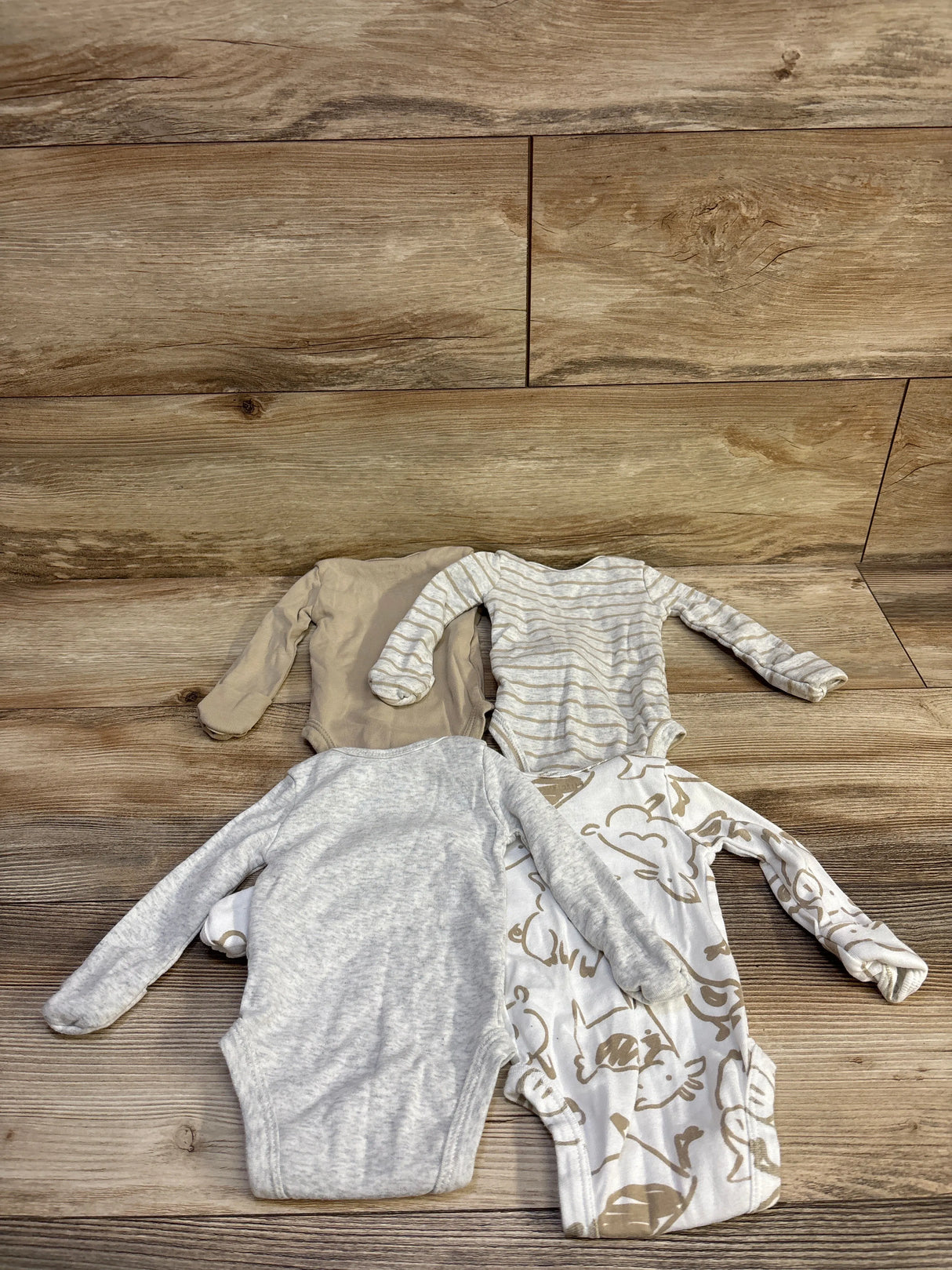 Flat lay of a 4-pack of newborn bodysuits in neutral grey and beige with stripes and animal print on wood background
