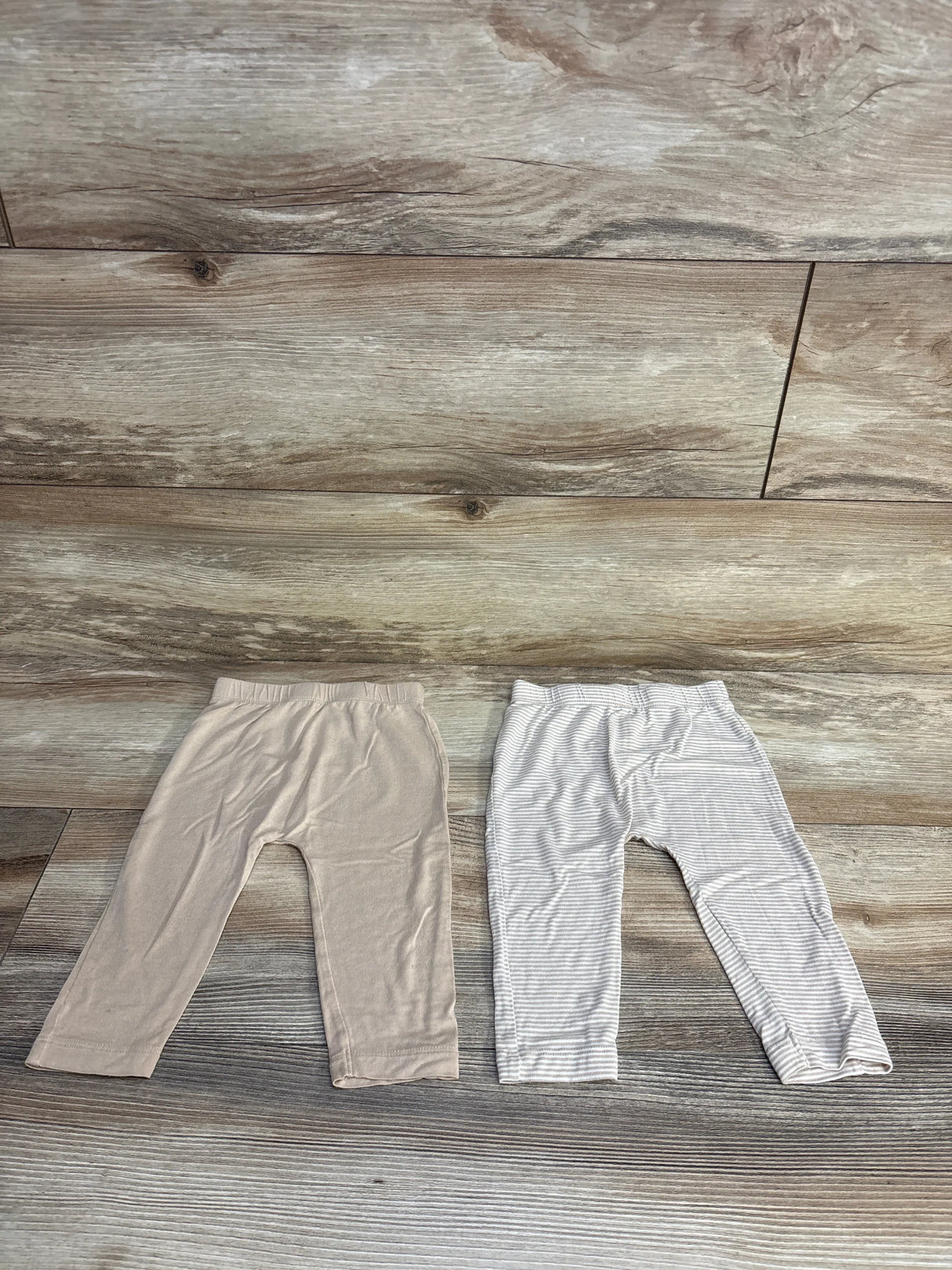 Two pairs of baby leggings, solid beige and gray striped, laid flat on wood floor for kids clothing resale