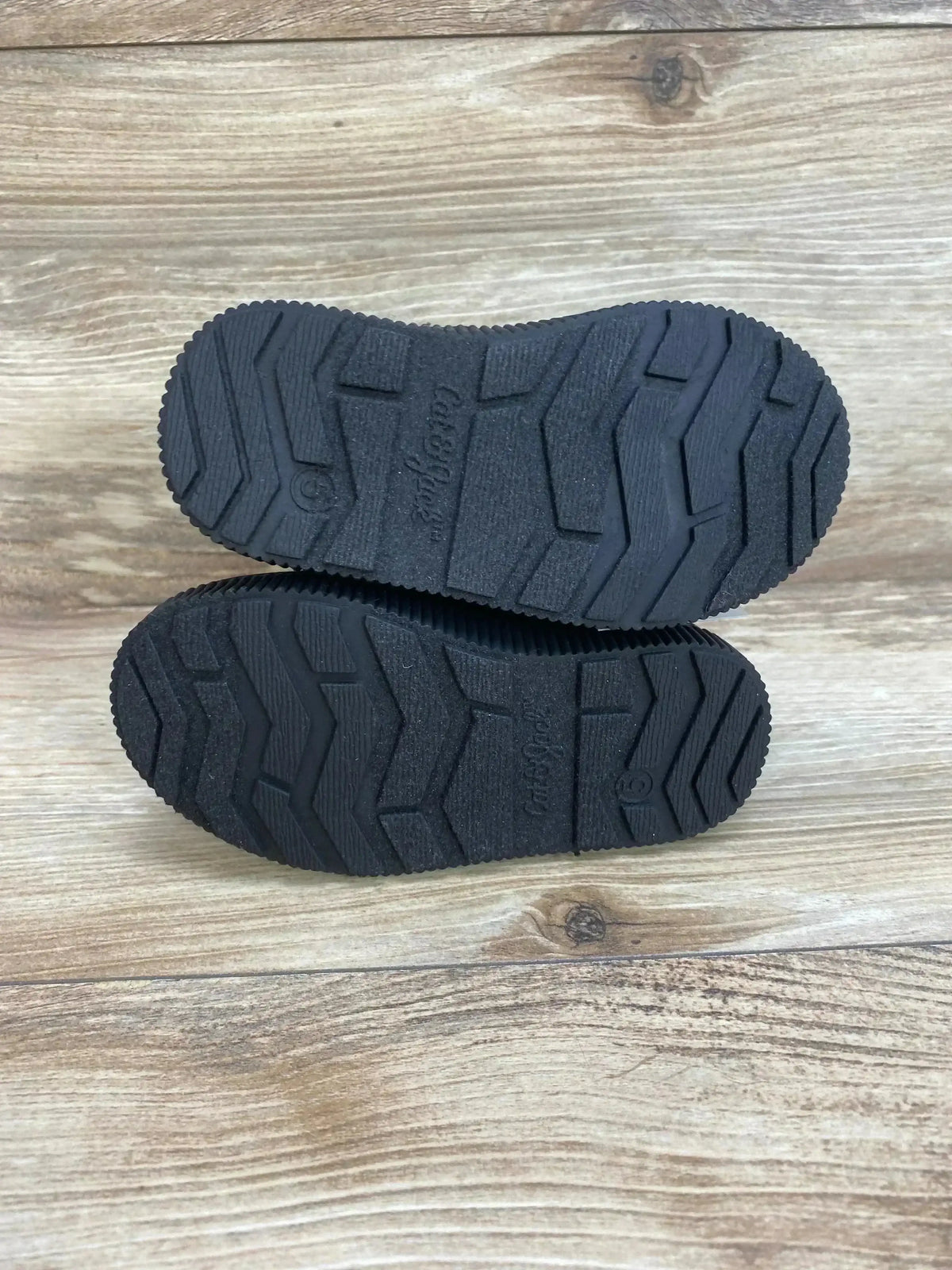 Bottom view of Cat & Jack Pip toddler boots showing black rubber tread pattern and embossed brand name on wood floor